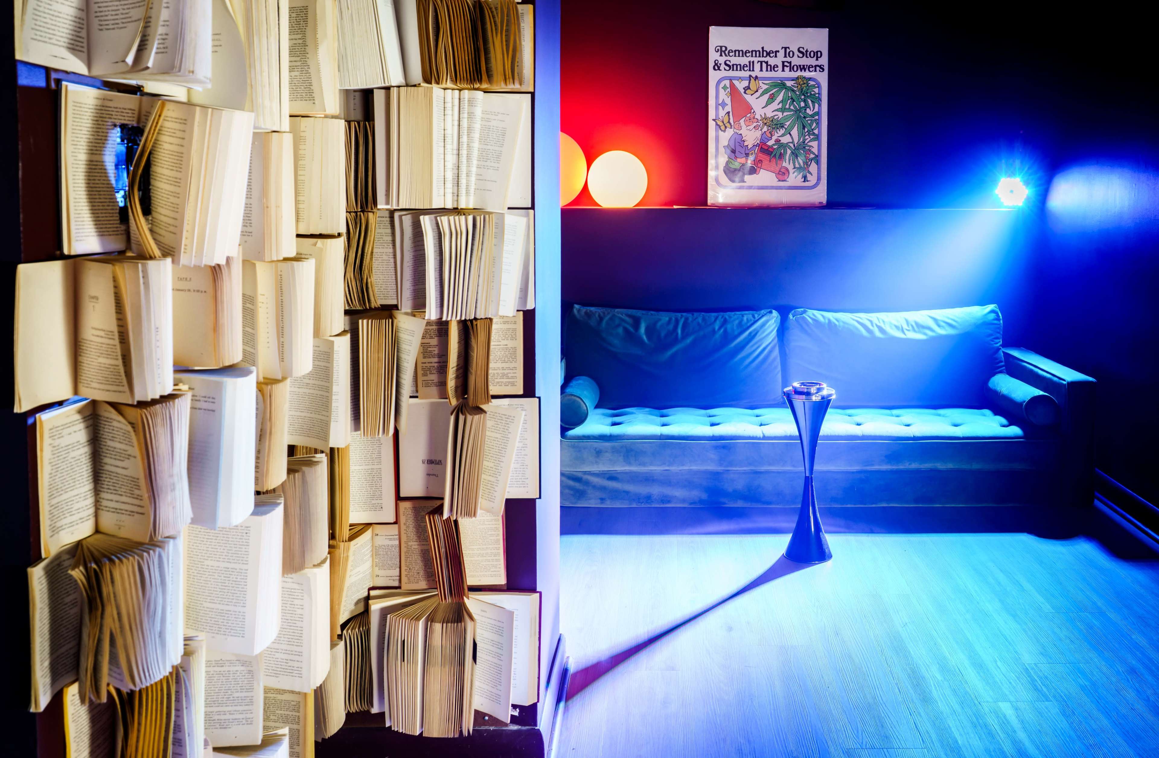 The scene features a dimly lit room with a wall of open books on one side and a cozy blue couch illuminated by colored lights on the other.