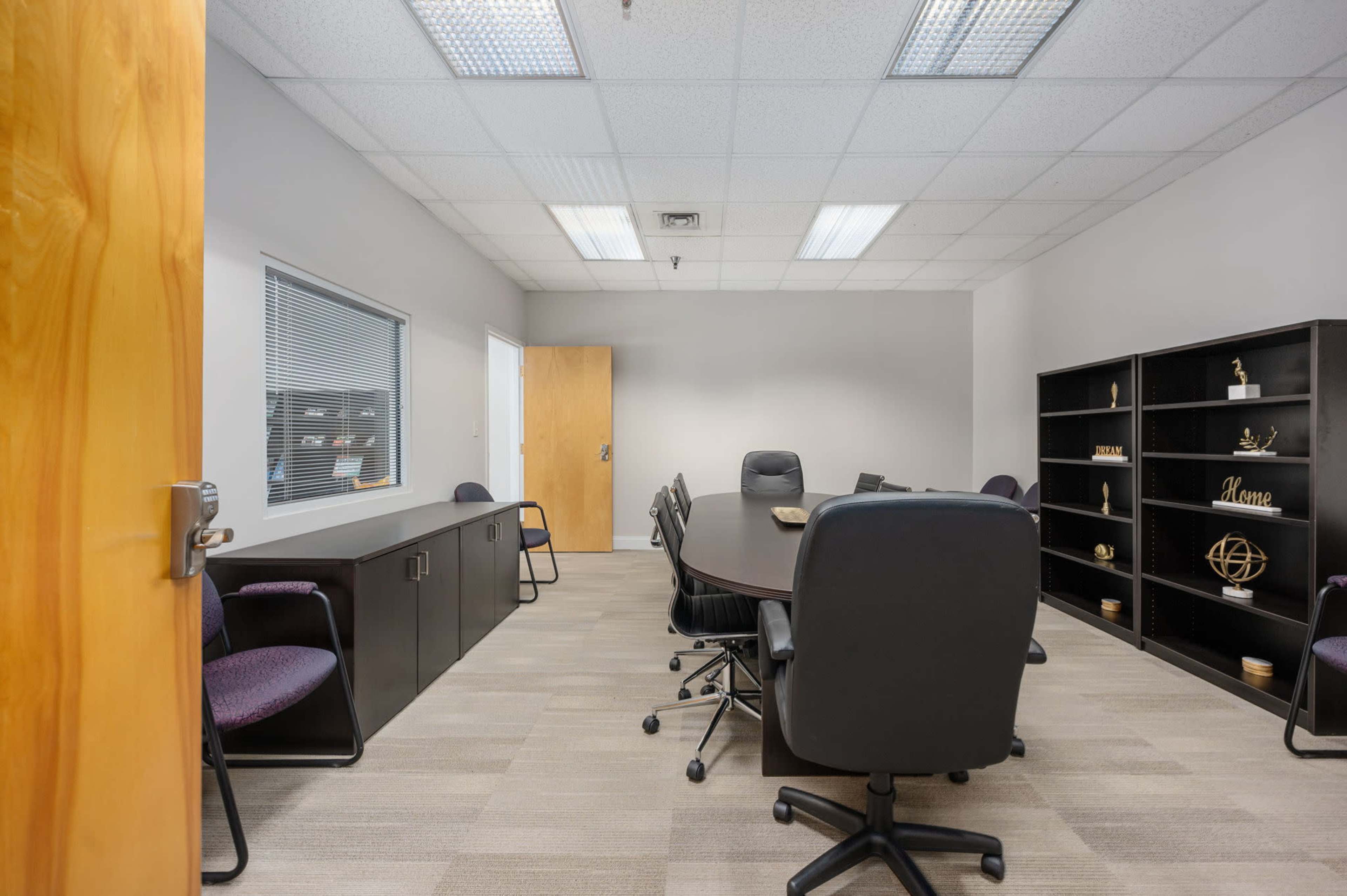 A conference room is set up with a large table surrounded by black chairs, and a storage cabinet lines one wall.