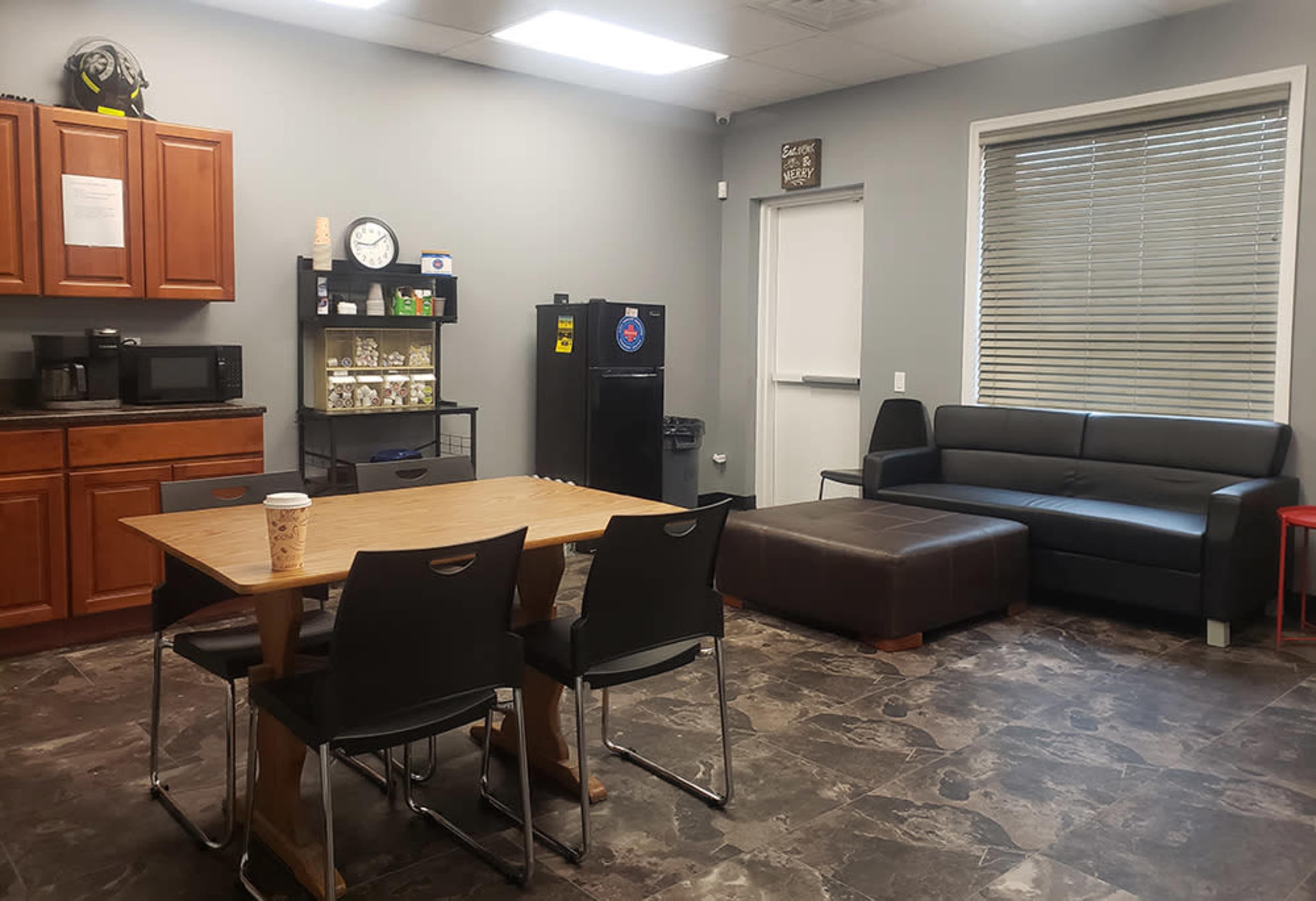A break room with a wooden table and black chairs, a black couch, and kitchen appliances including a microwave and refrigerator.