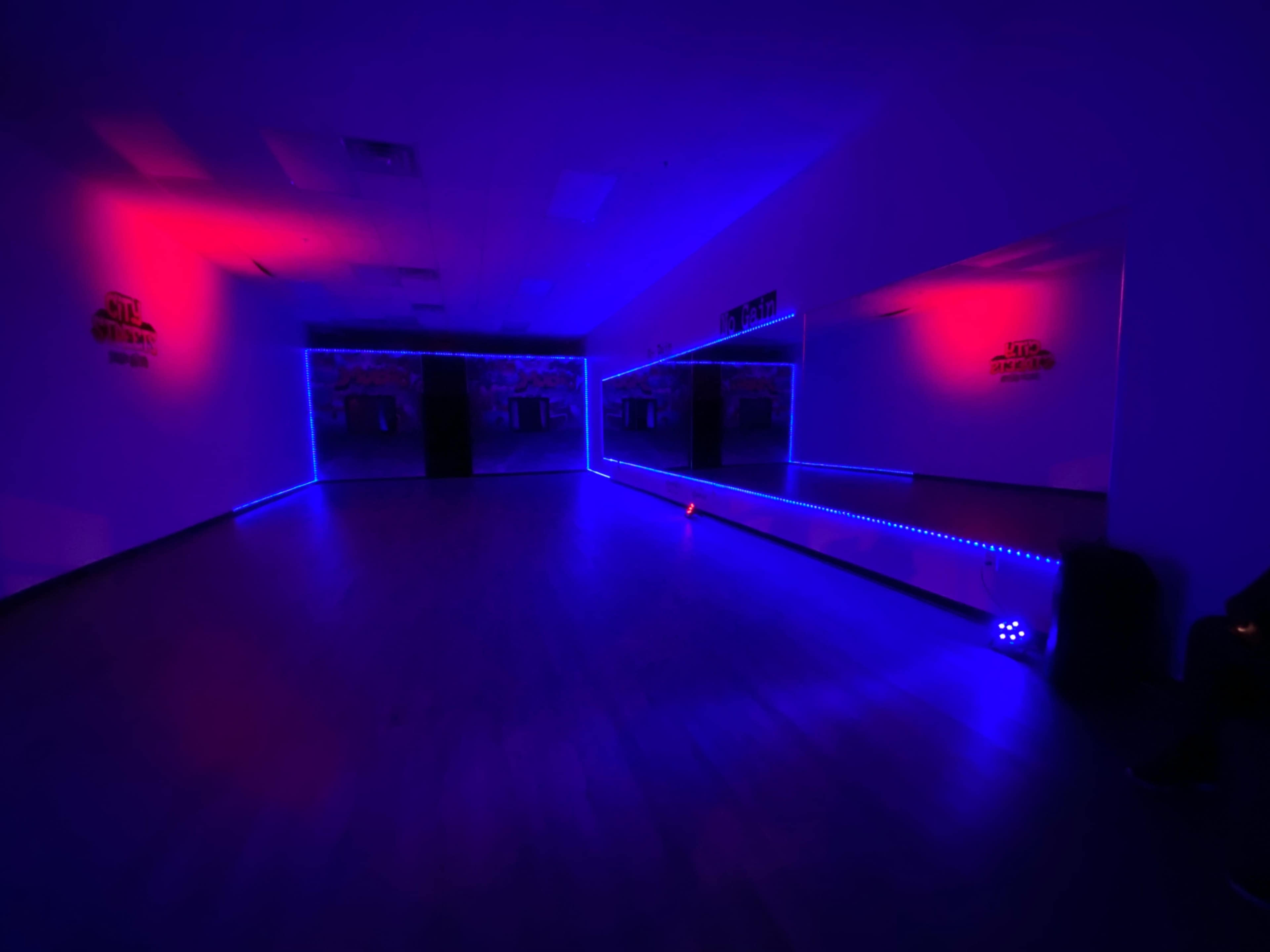 A dimly lit dance studio with blue and red LED lighting and a large mirror on one wall.