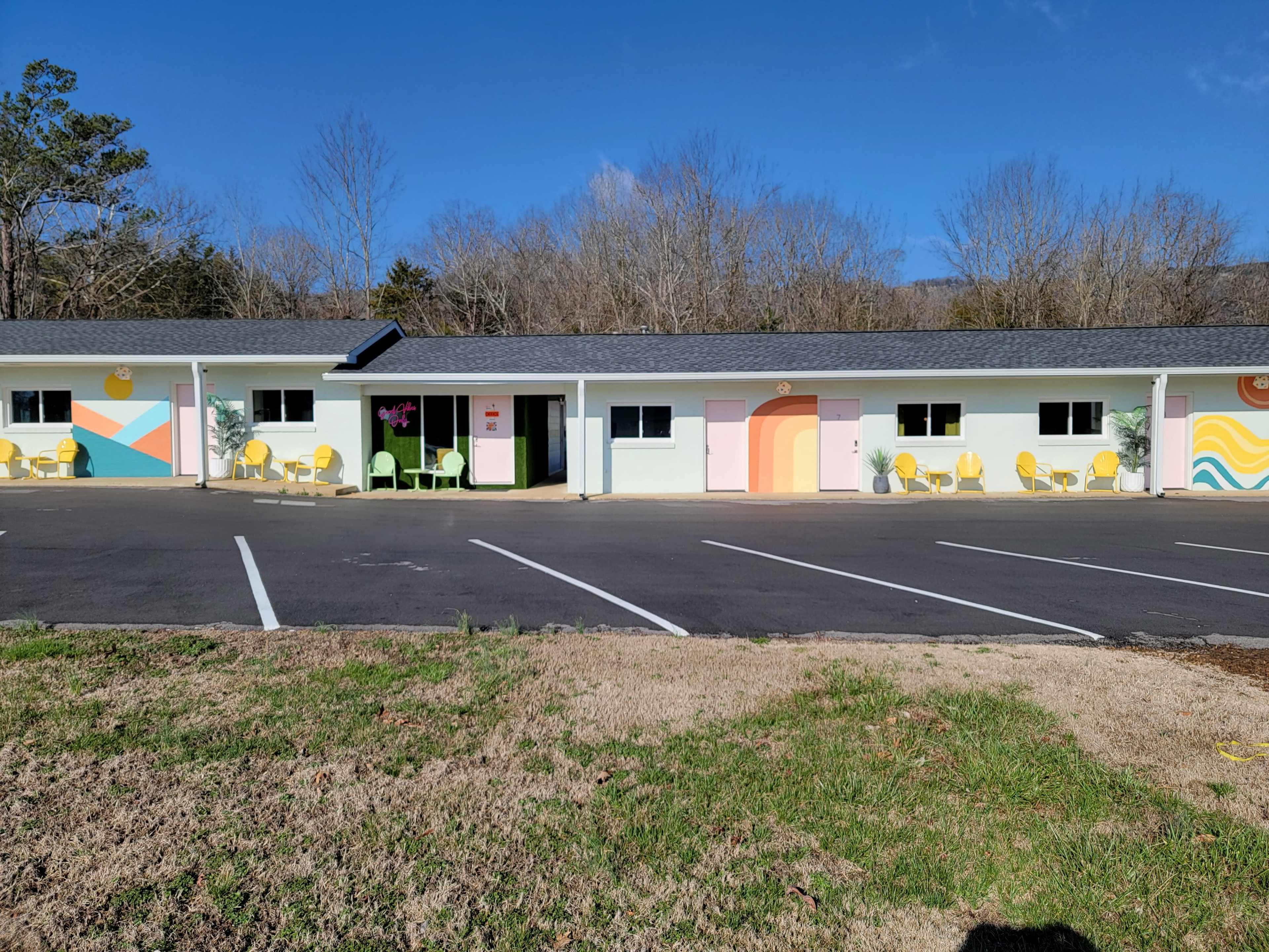 A colorful motel features pastel walls with murals and outdoor seating areas, set against a clear blue sky.