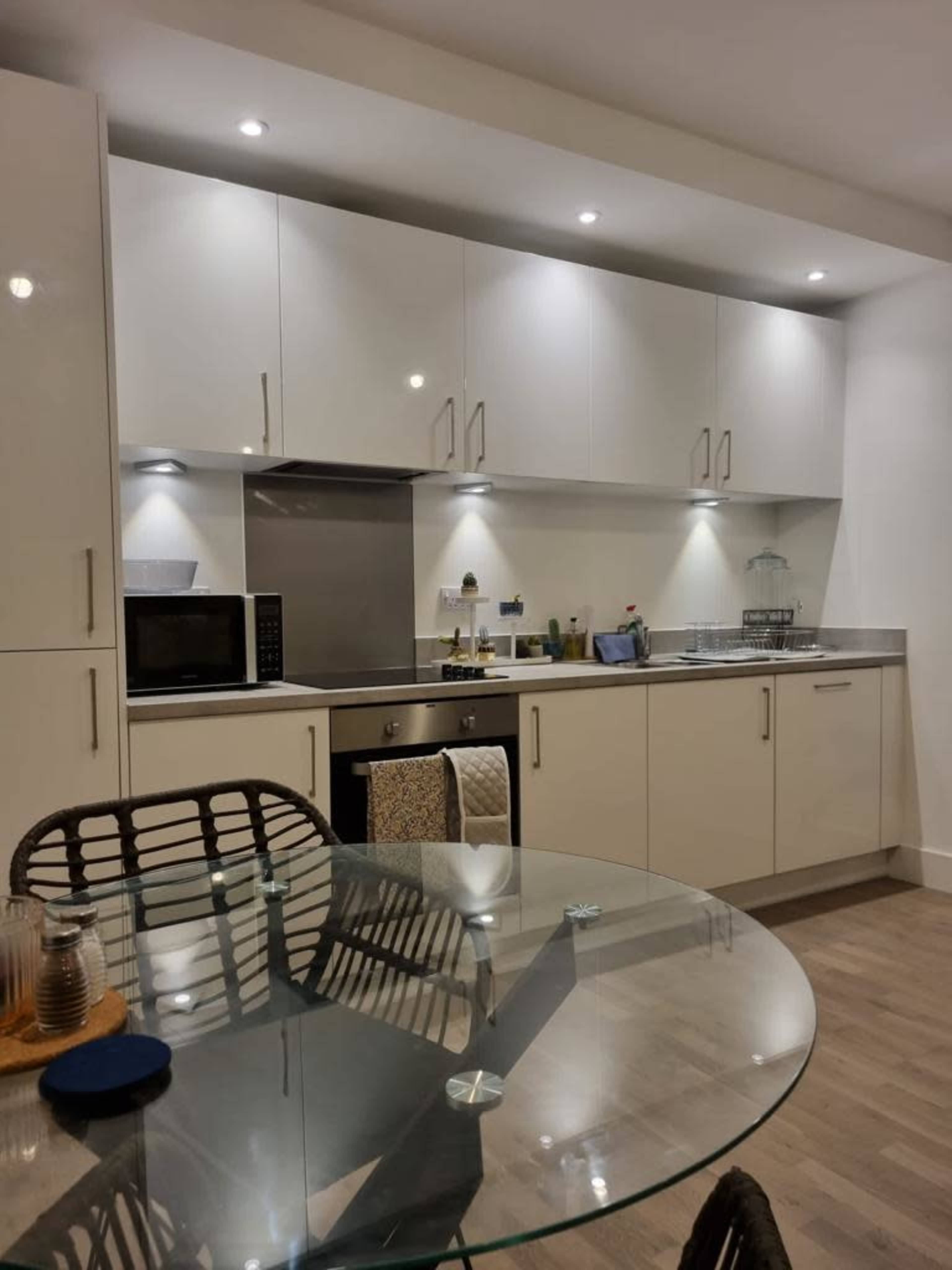 The image shows a modern kitchen with sleek white cabinetry, stainless steel appliances, and a glass dining table.