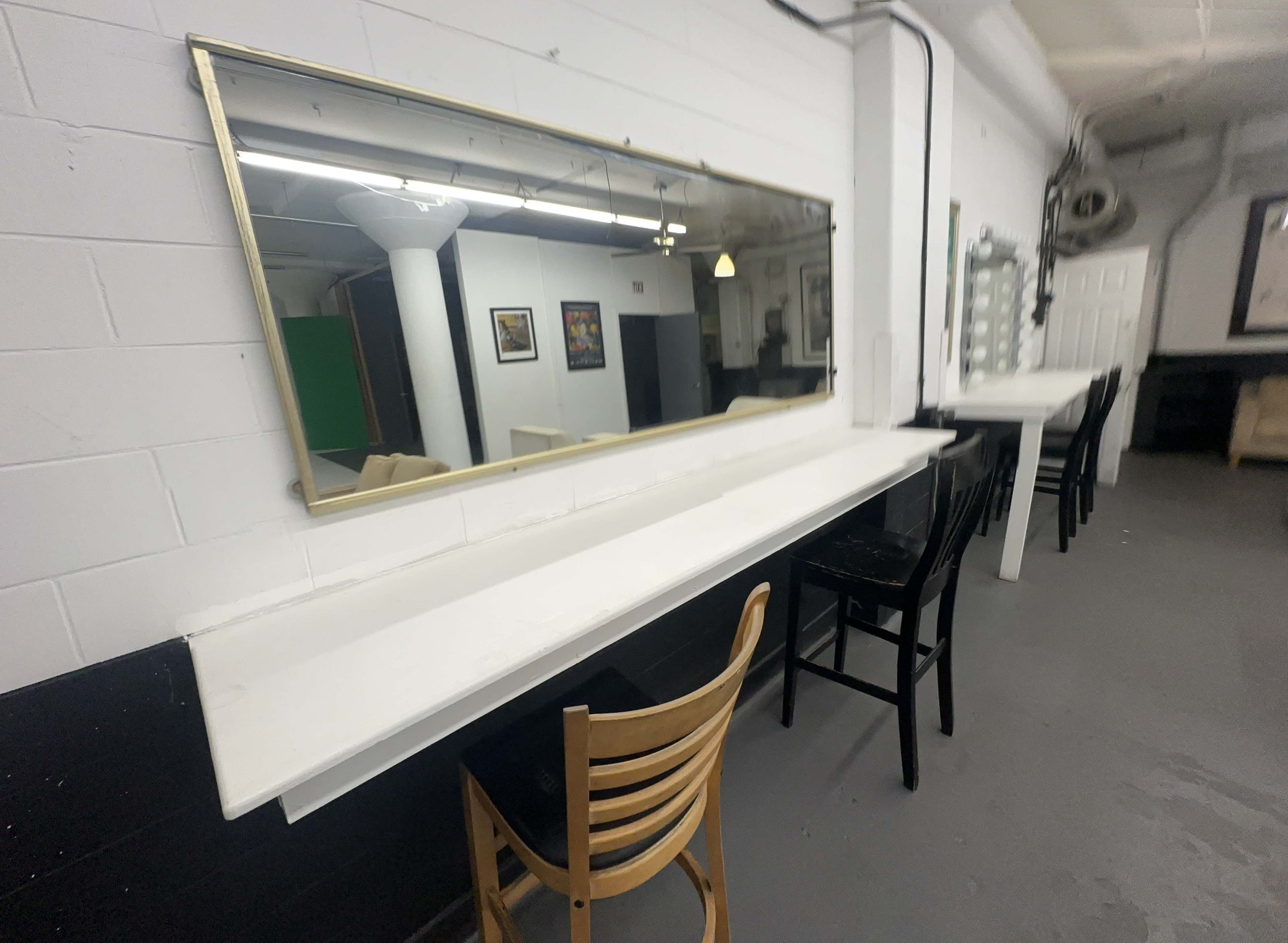 A long white countertop with two wooden chairs and a large mirror mounted above it, set in a room with black and white walls.