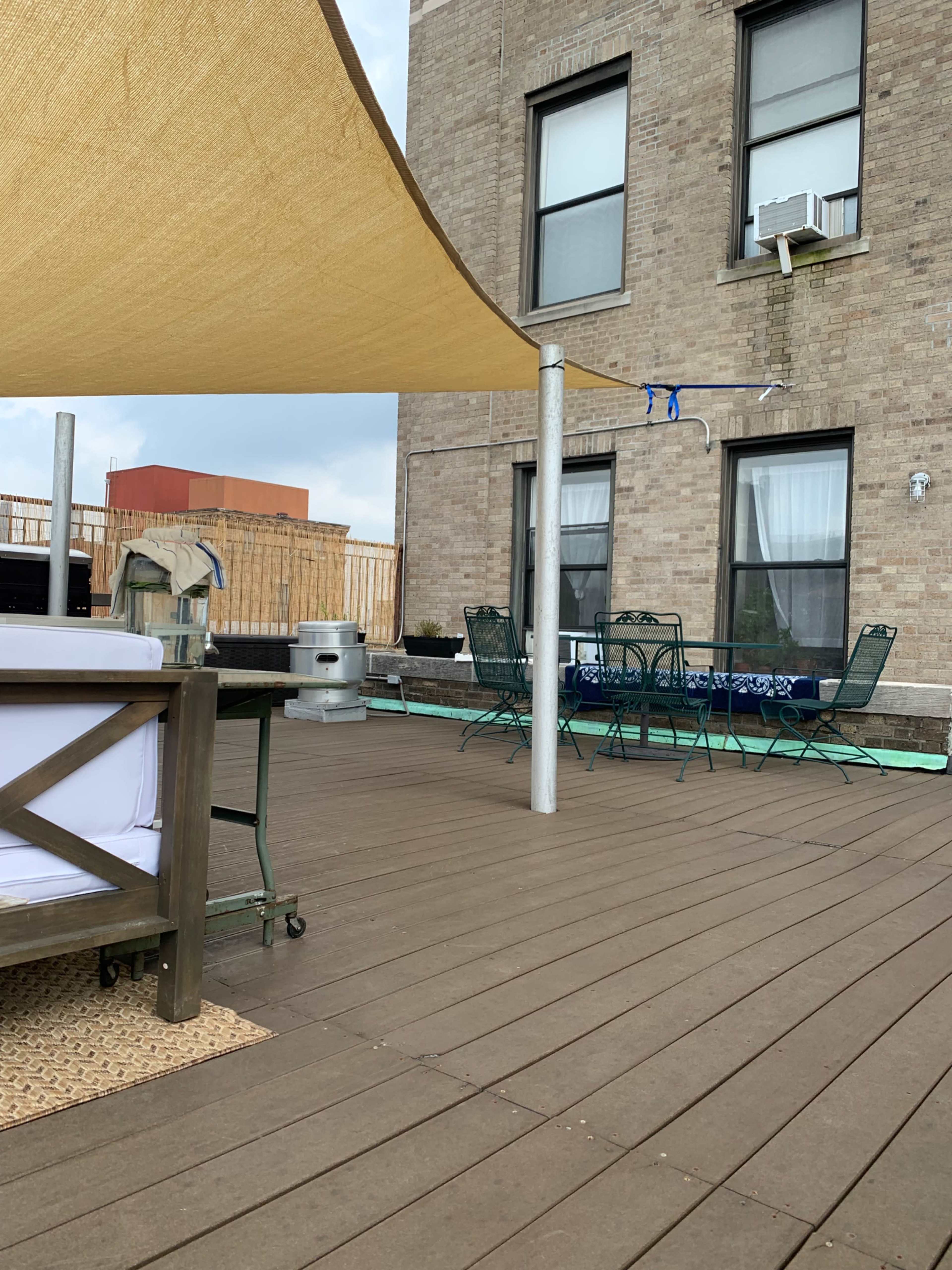 A rooftop patio with a wooden deck, a shaded seating area, and a table with chairs near the building's brick exterior.