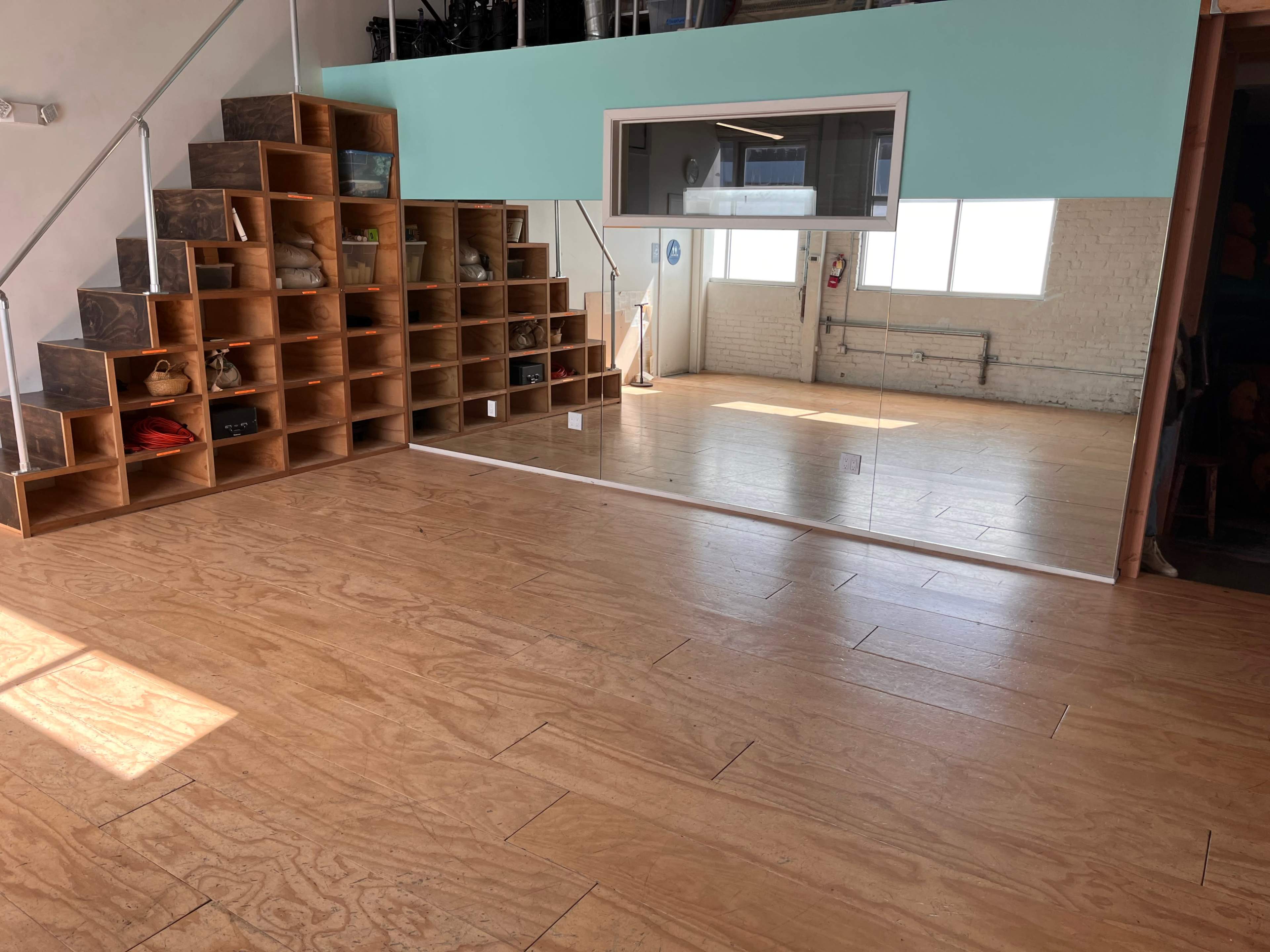 A spacious room with wooden flooring, featuring a large mirror on one wall and a set of open shelves arranged in a staircase design on another.