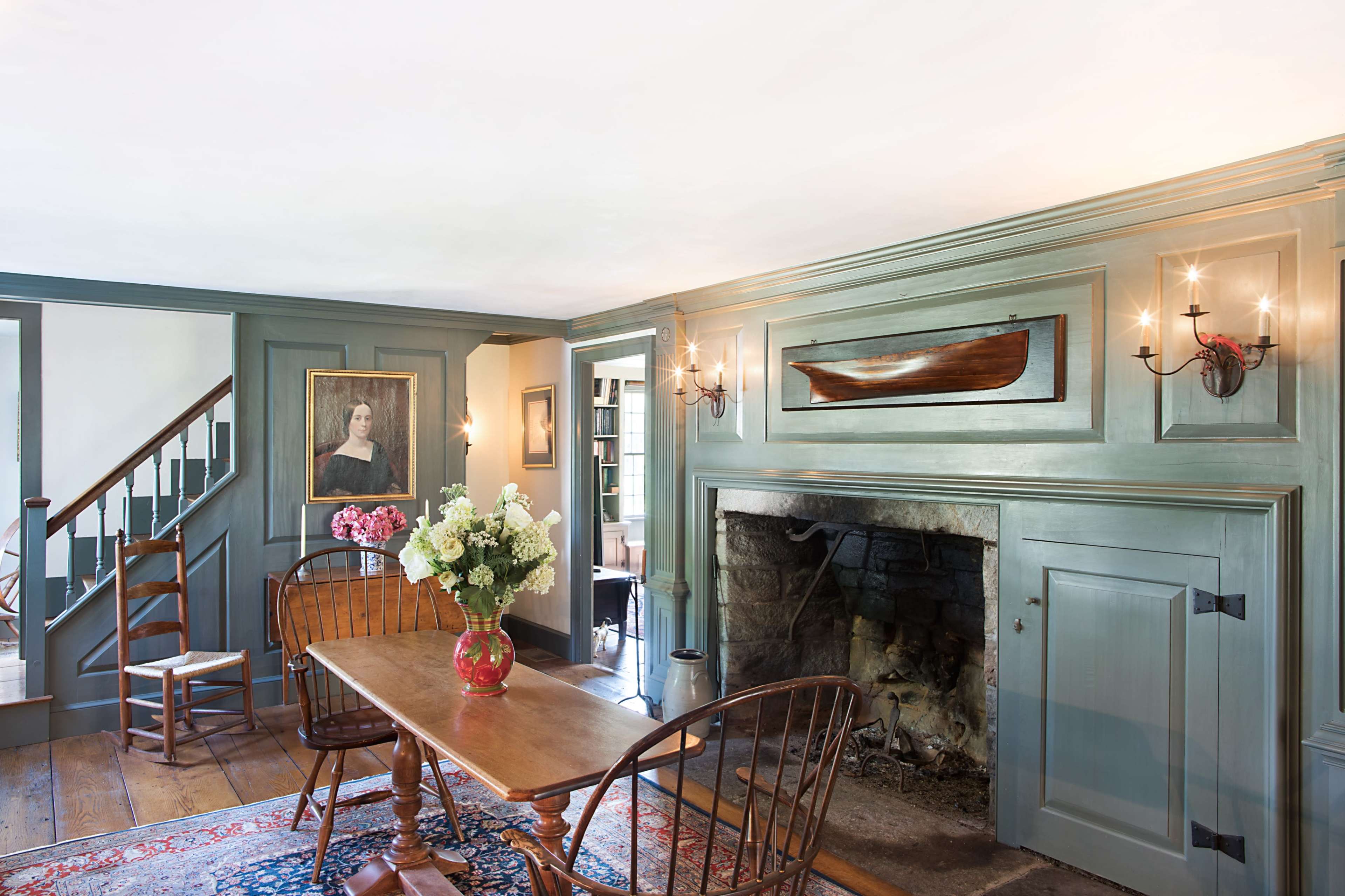 A cozy, well-lit room with a wooden table and chairs, a large fireplace, and a staircase leading to another level.