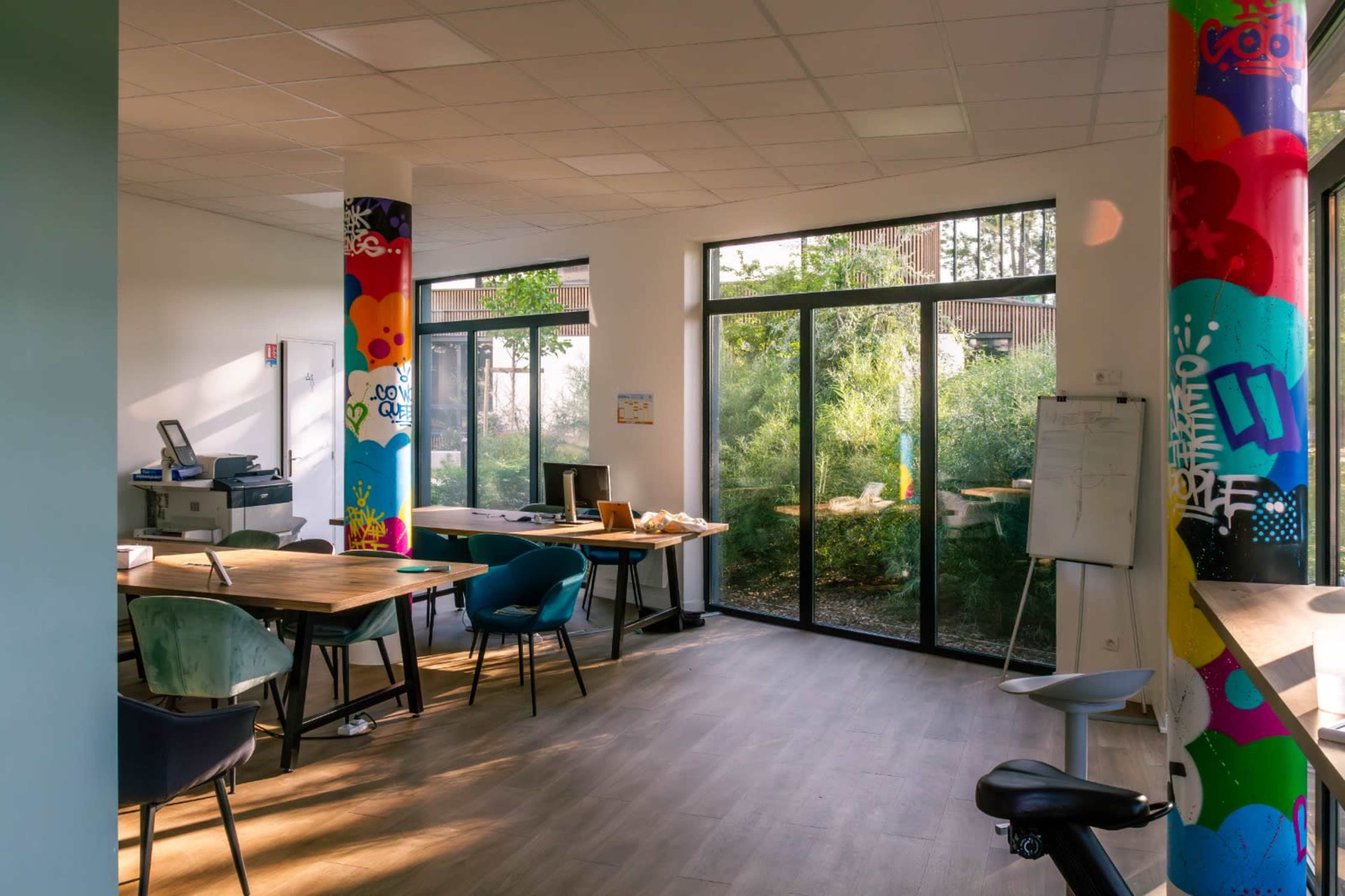 A modern office space featuring large windows, a printer, and colorful pillars adorned with graffiti-style designs.