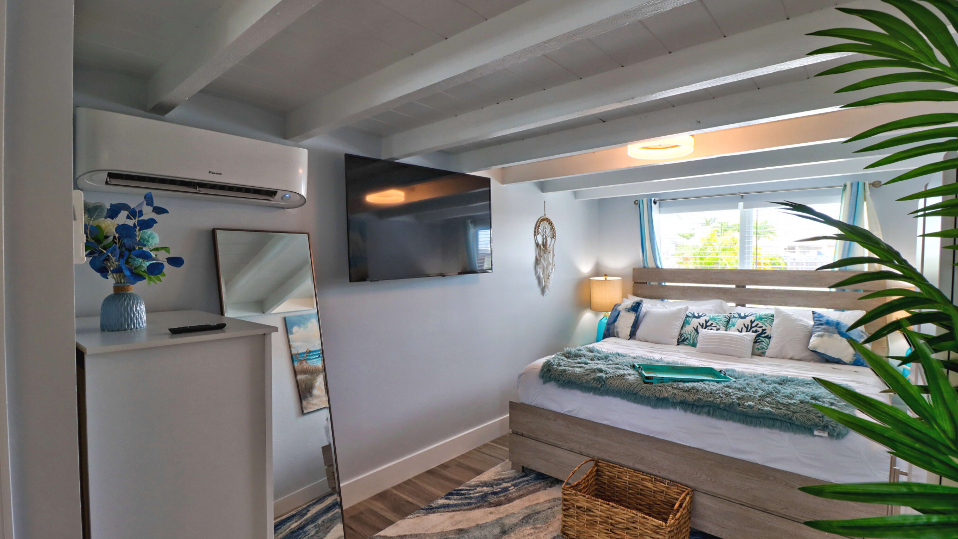 A cozy bedroom with a double bed, a large mirror, a mounted television, and a decorative plant in the corner.