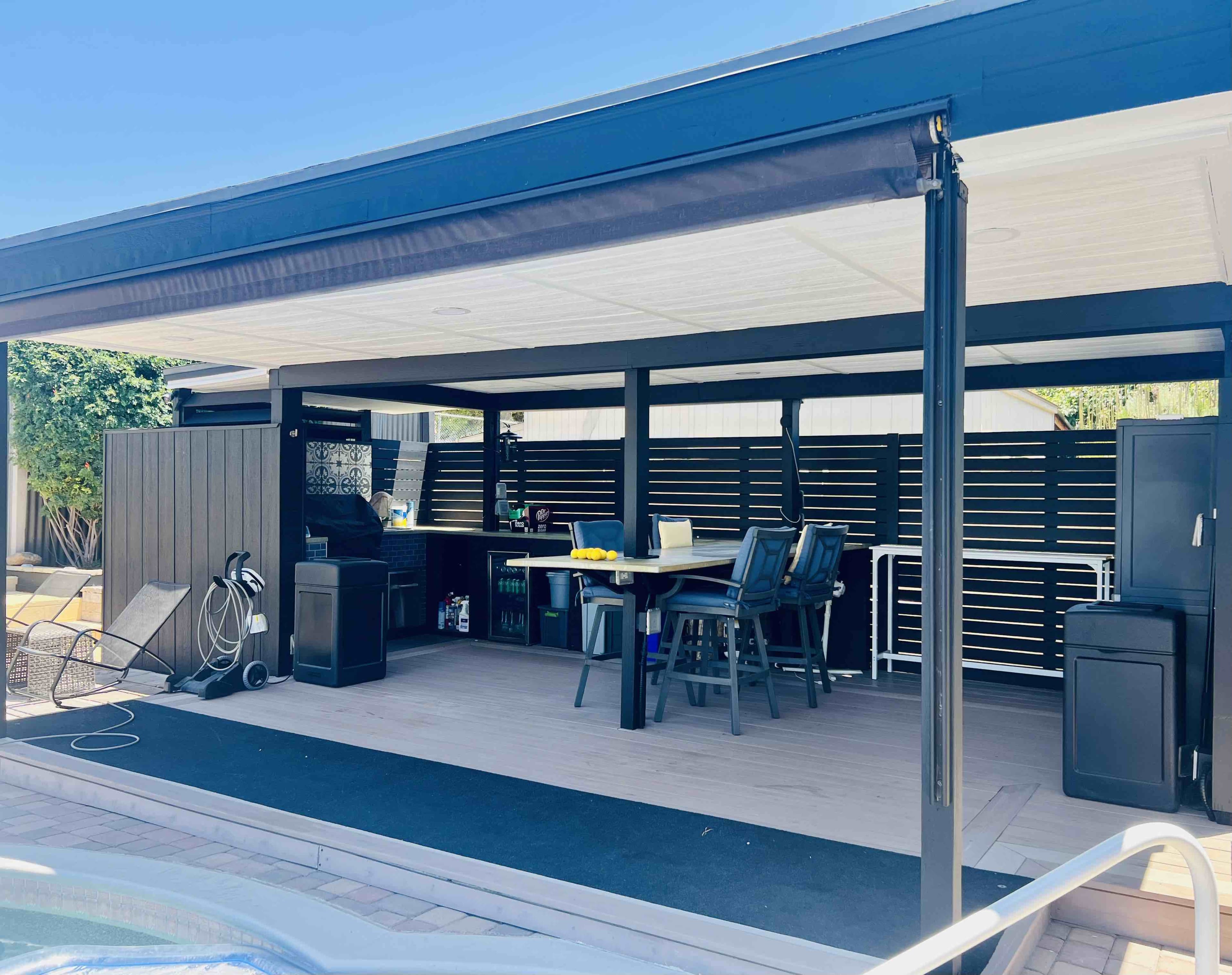 The image shows a covered outdoor kitchen area with seating, a bar counter, and various appliances.