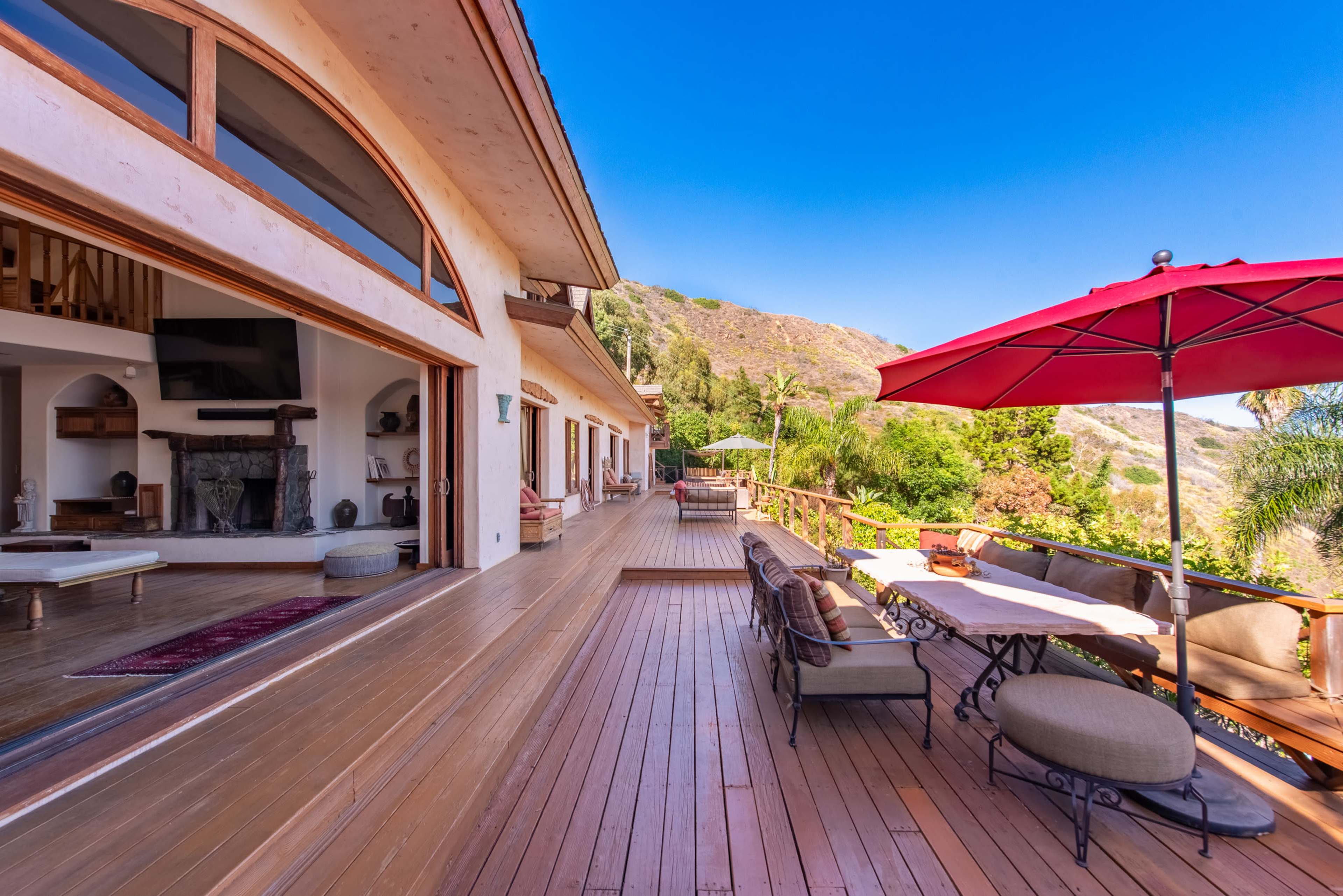 A spacious wooden deck of a house with an outdoor dining area and a view of a hillside landscape.