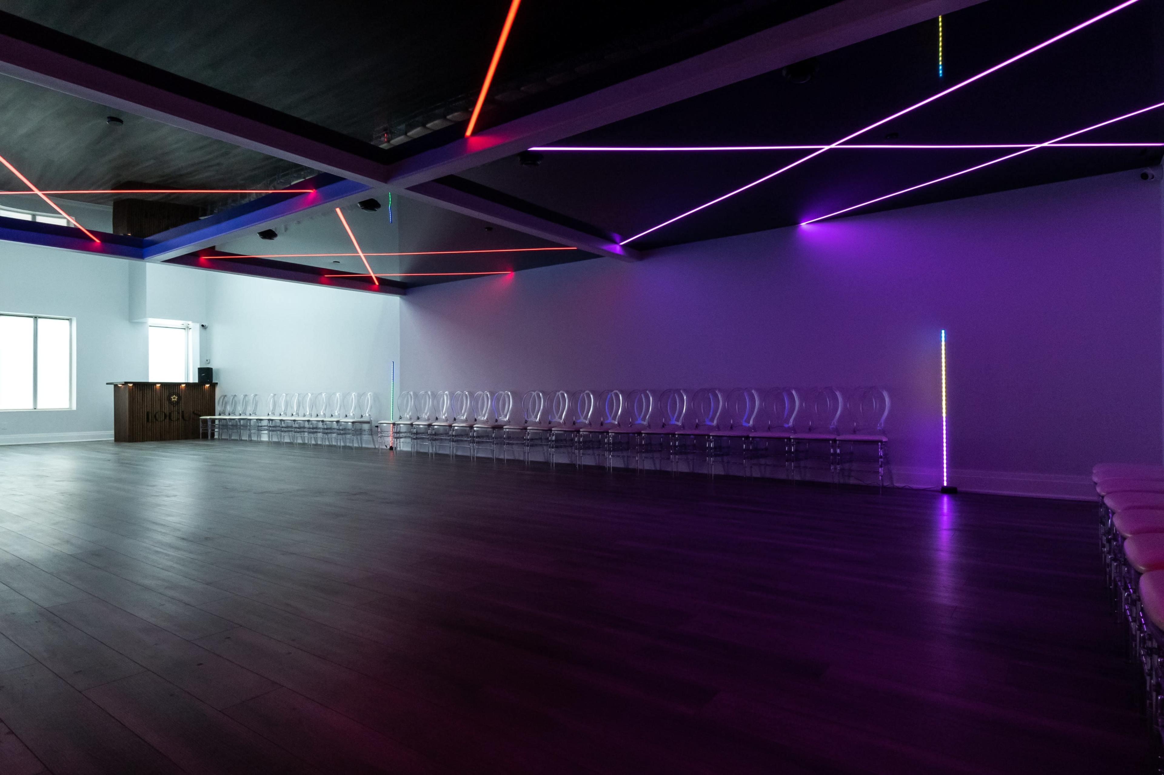 A spacious room with clear chairs arranged in a row and colorful LED lights illuminating the ceiling.