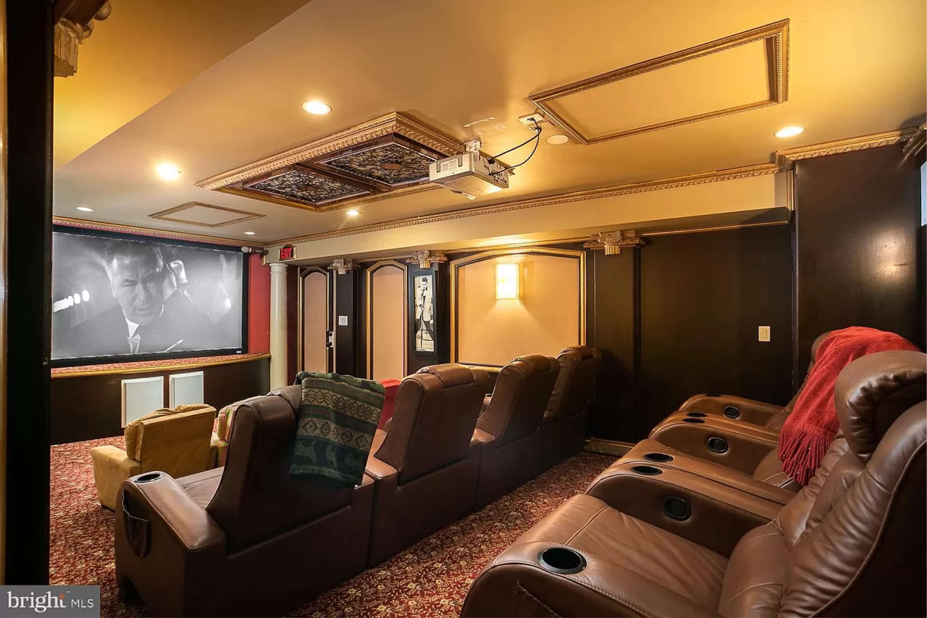 A home theater with reclining leather chairs facing a large screen and a projector mounted on the ceiling.