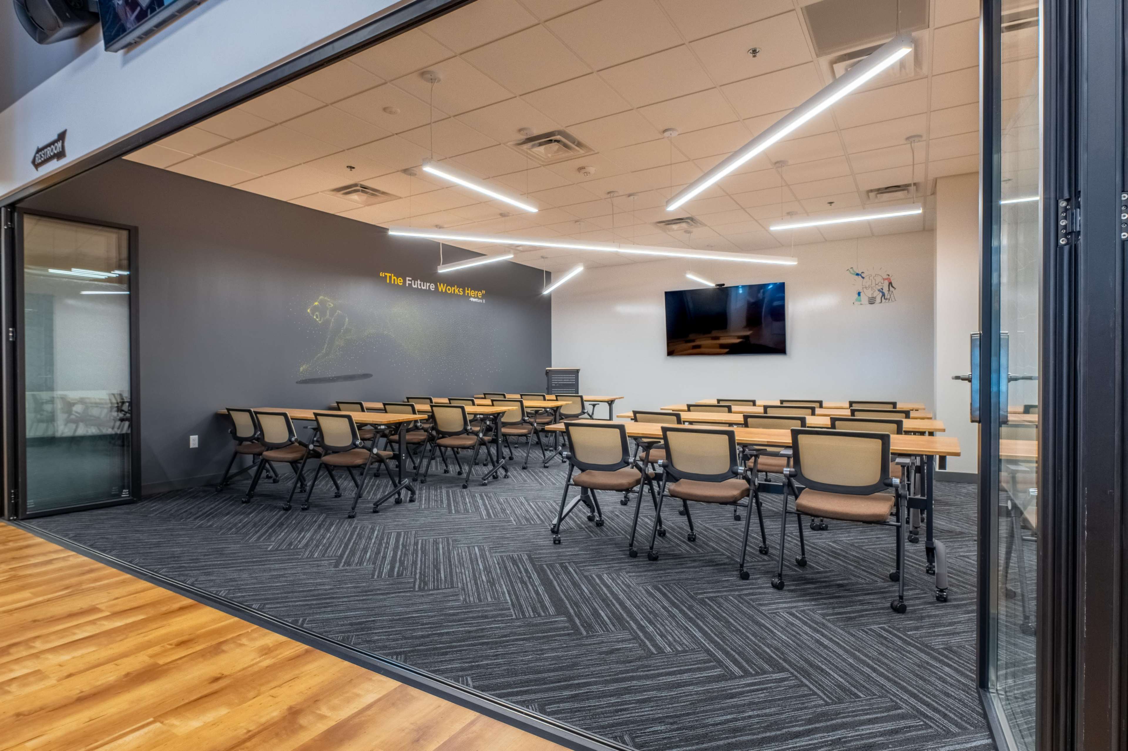 A classroom with rows of tables and chairs, a projector screen at the front, and quote artwork on the wall.