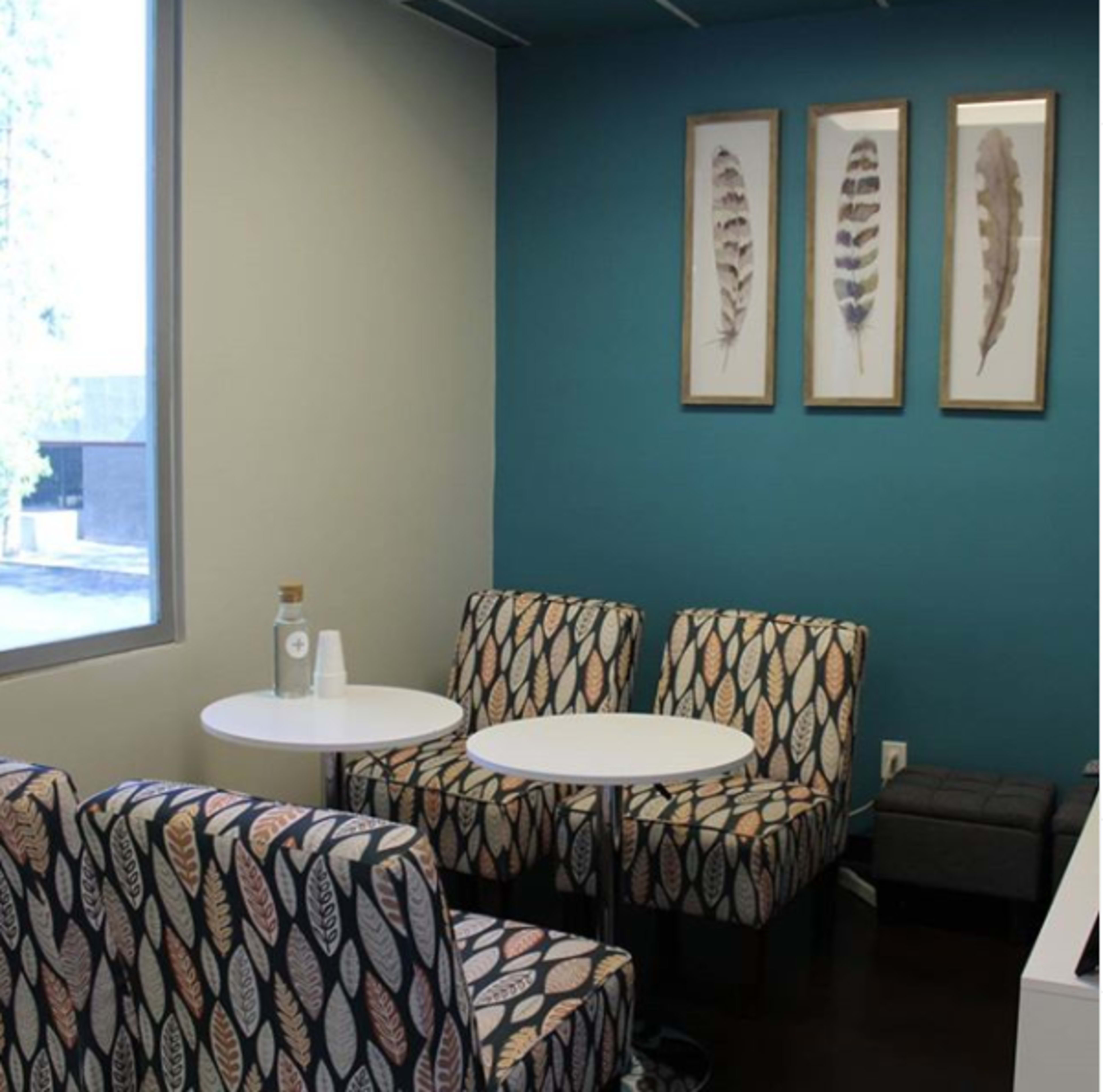 A small seating area with two patterned chairs and a round table against a blue wall adorned with framed feather artwork.