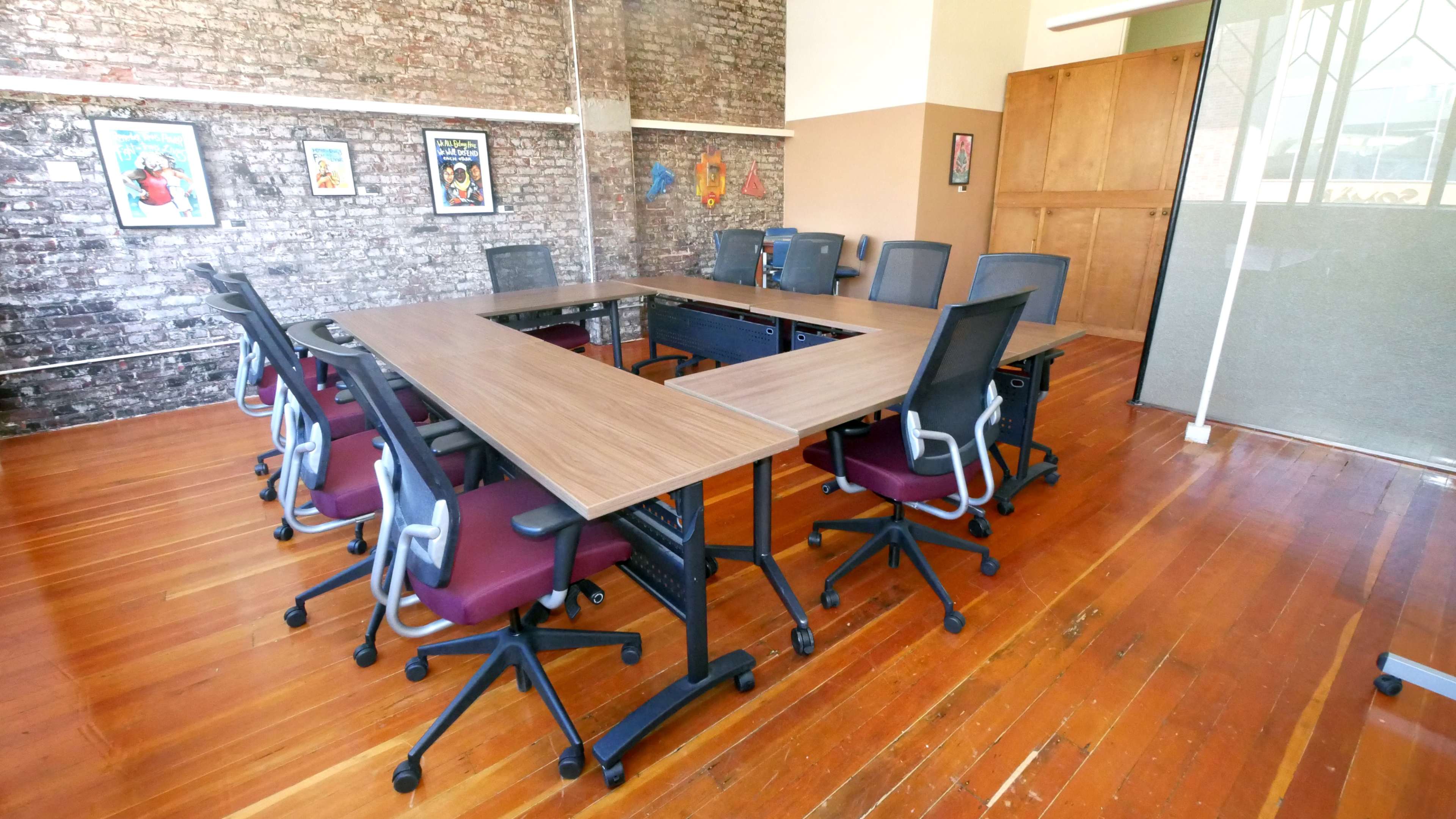 A conference room features a large rectangular table surrounded by several chairs, against a backdrop of brick walls adorned with posters.