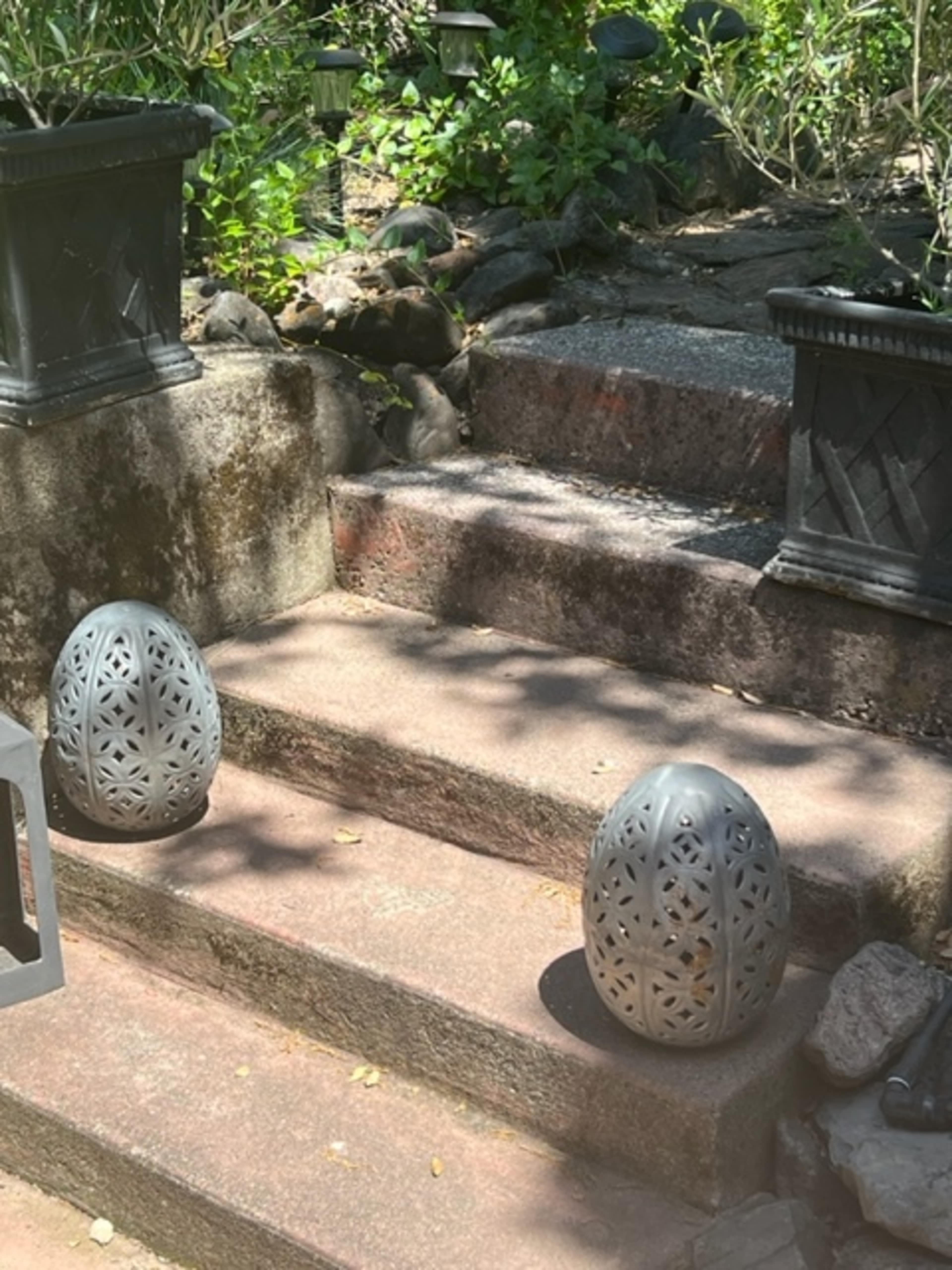 Two patterned, gray lanterns are positioned on each side of stone steps in a garden setting.