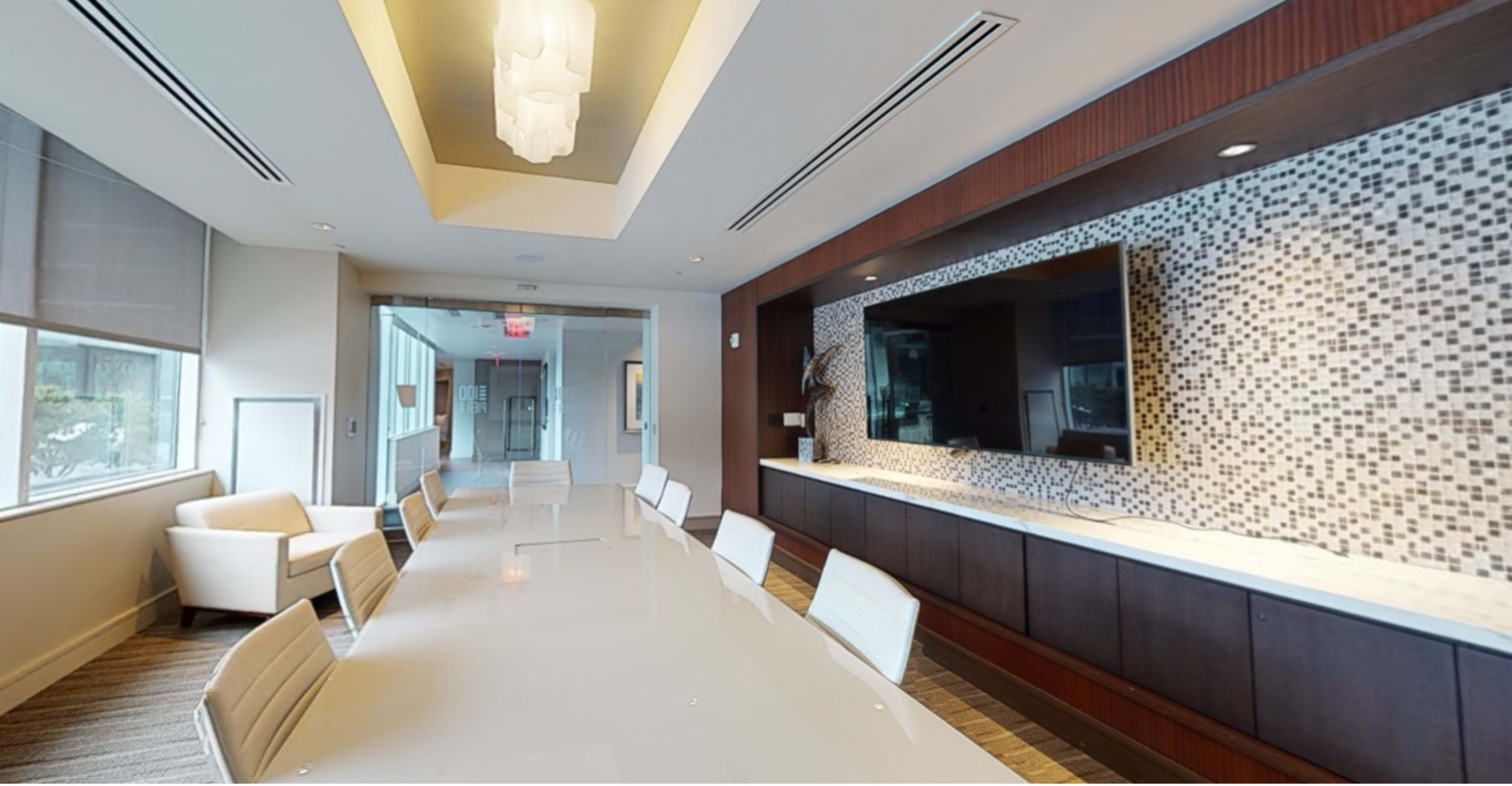 A modern conference room with a long white table, white chairs, and a decorative wall featuring a TV and mosaic tiles.