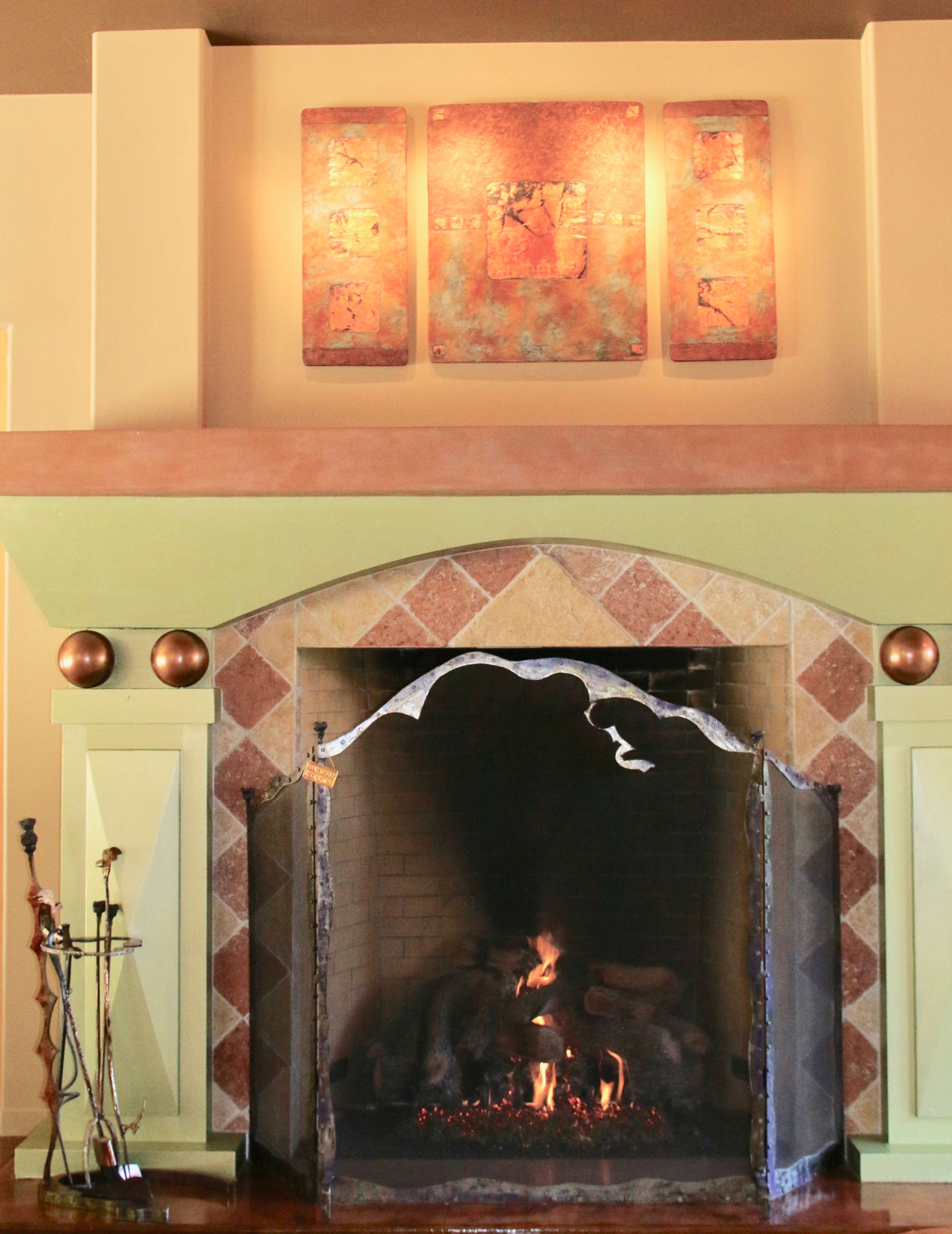 A stone fireplace with a metal screen displays a fire, surrounded by a decorated mantel and wall art.