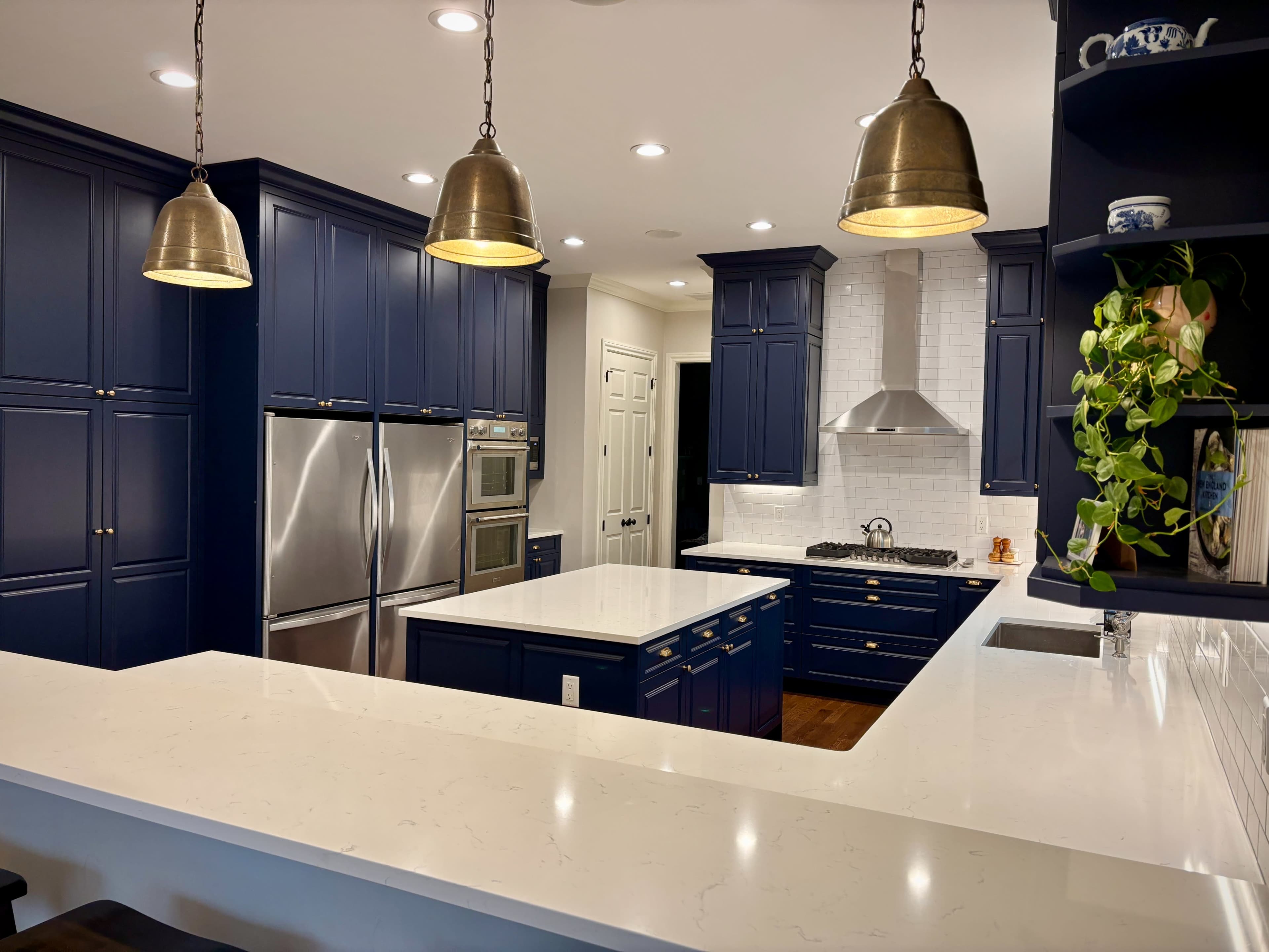 The image shows a modern kitchen with navy blue cabinets, stainless steel appliances, and a white quartz countertop.