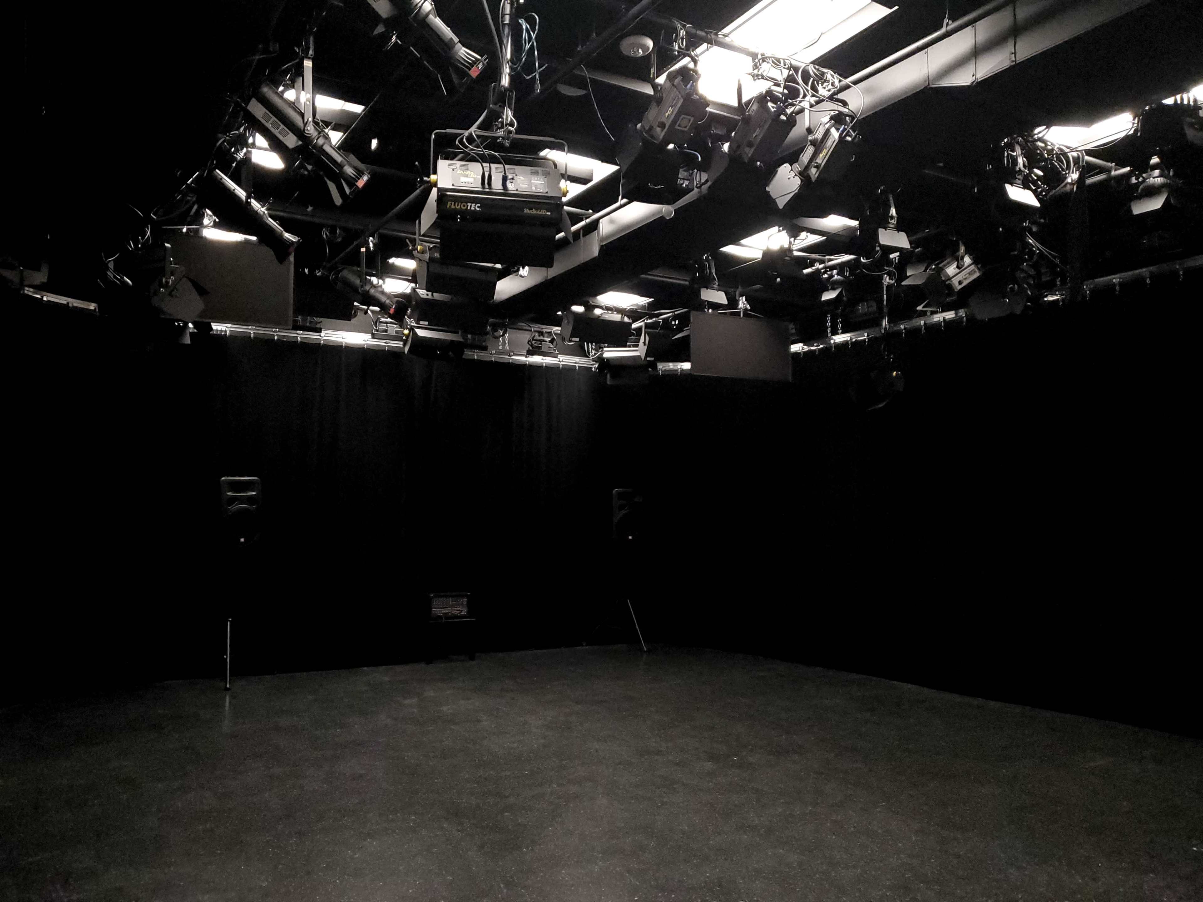 A dimly lit studio space equipped with overhead lighting and sound speakers in a dark environment.