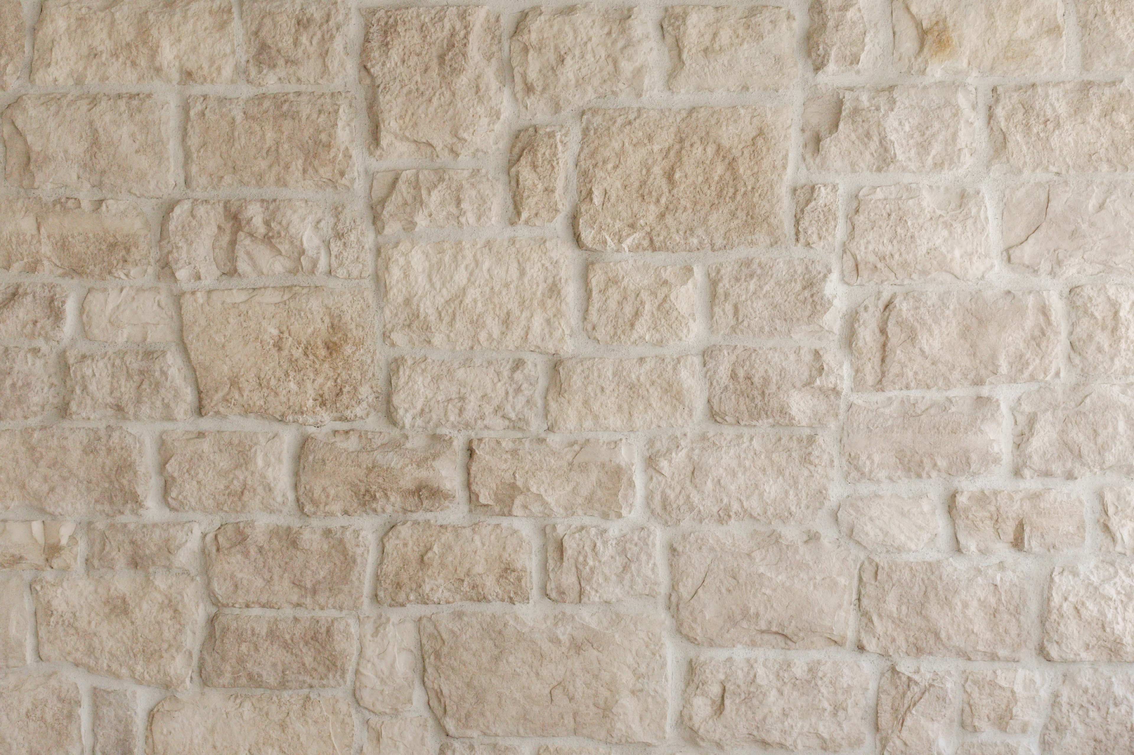 The image shows a textured wall made of light-colored stone bricks arranged in a random pattern.
