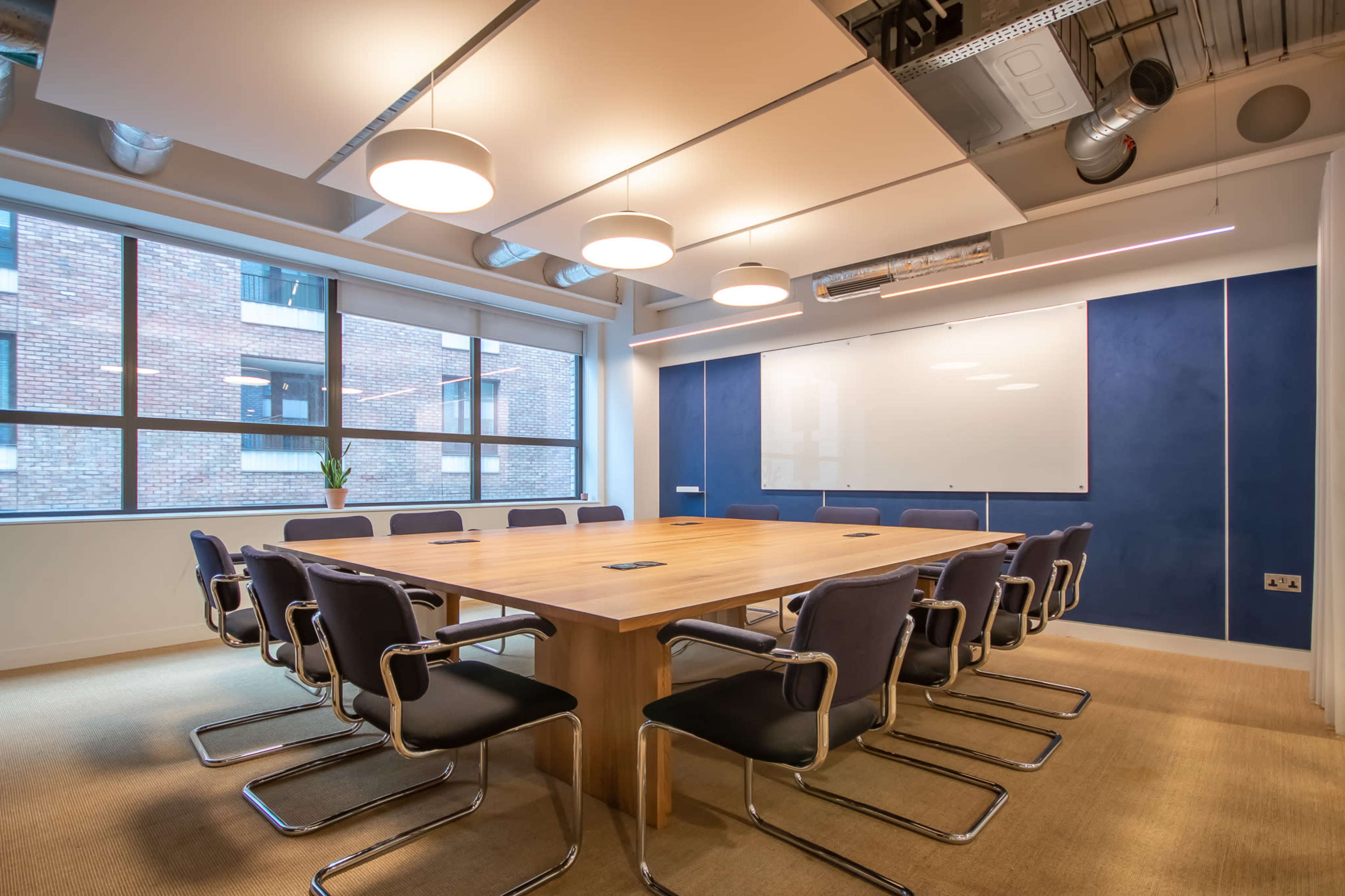 The image shows a modern conference room with a large wooden table surrounded by black chairs, large windows, and a whiteboard on the wall.