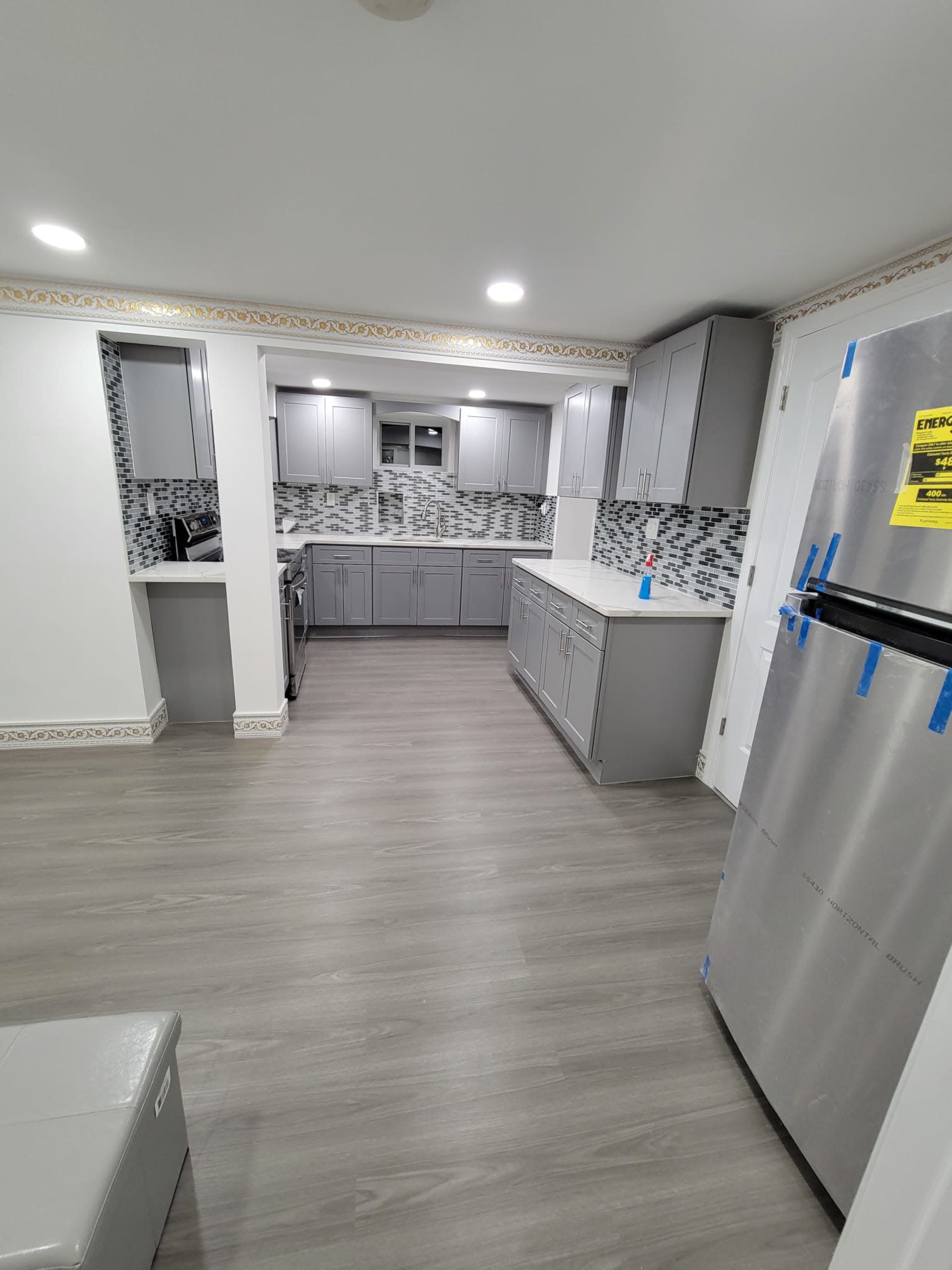 A modern kitchen with gray cabinets, a tiled backsplash, and stainless steel appliances, featuring a spacious layout with a light hardwood floor.