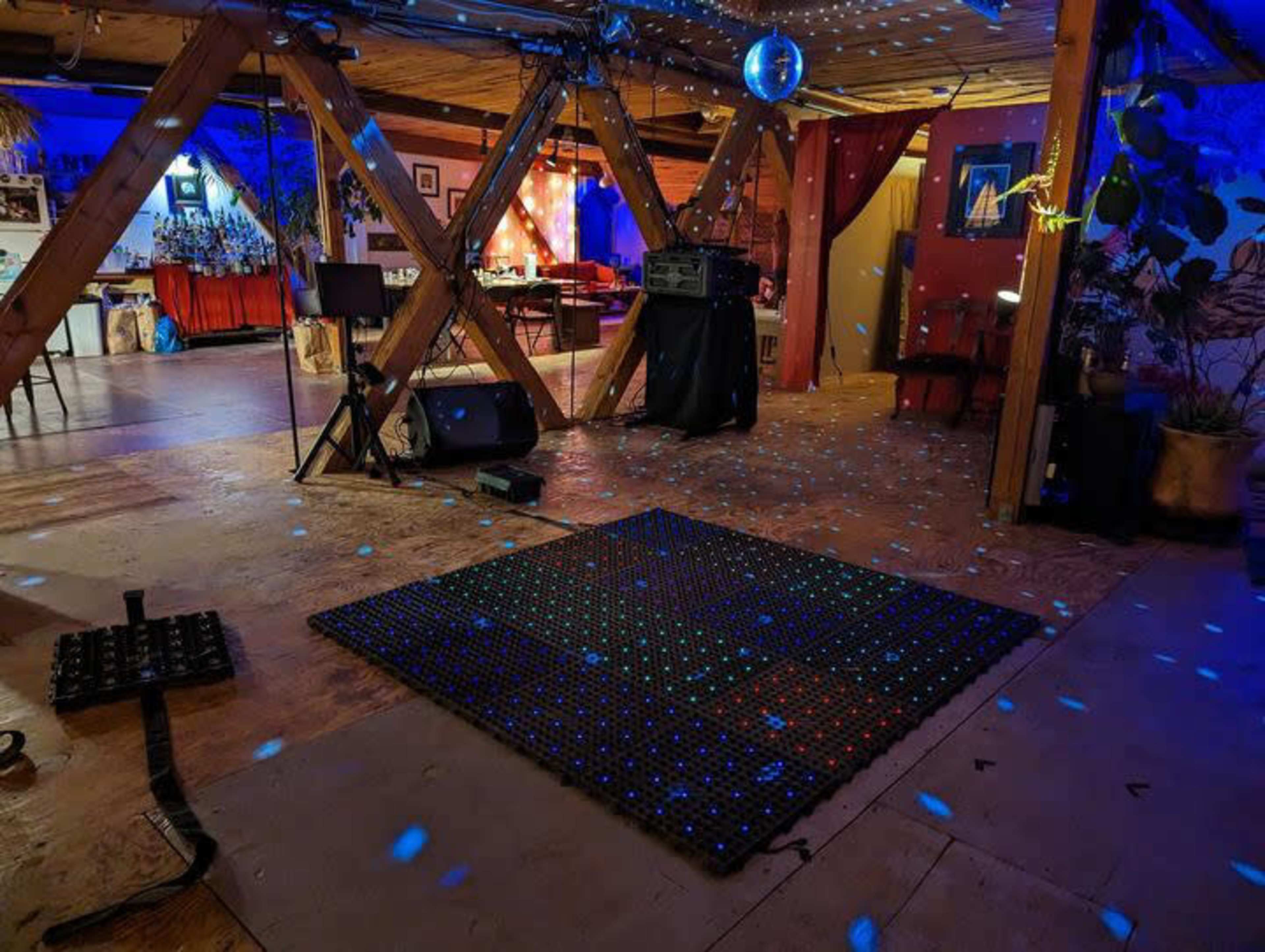 The image shows an empty dance floor area in a dimly lit venue with a disco ball and colorful lights scattered across the floor.