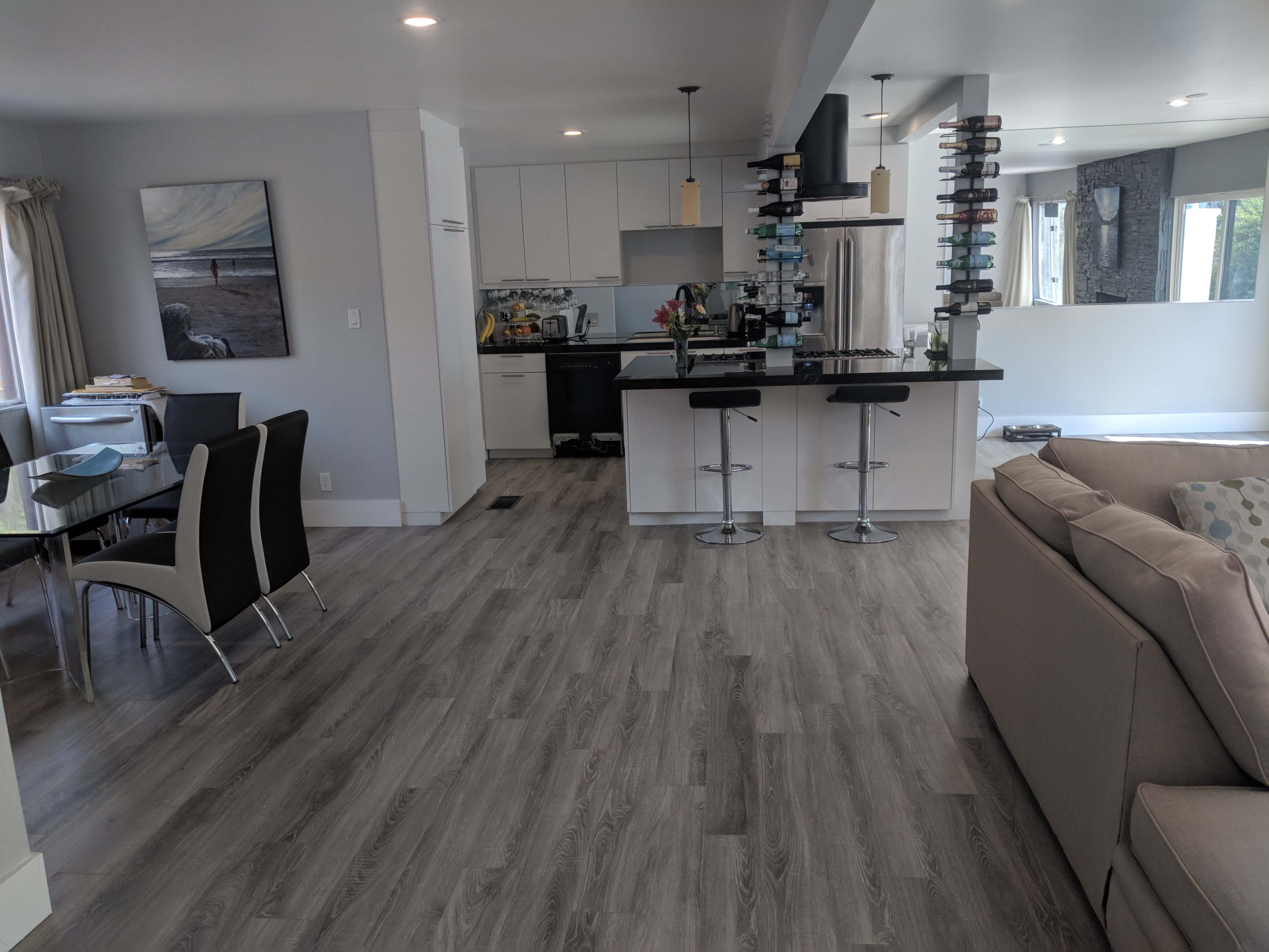 A modern open-concept living area featuring a kitchen with a bar, dining area with a glass table, and a comfortable living room with a couch.