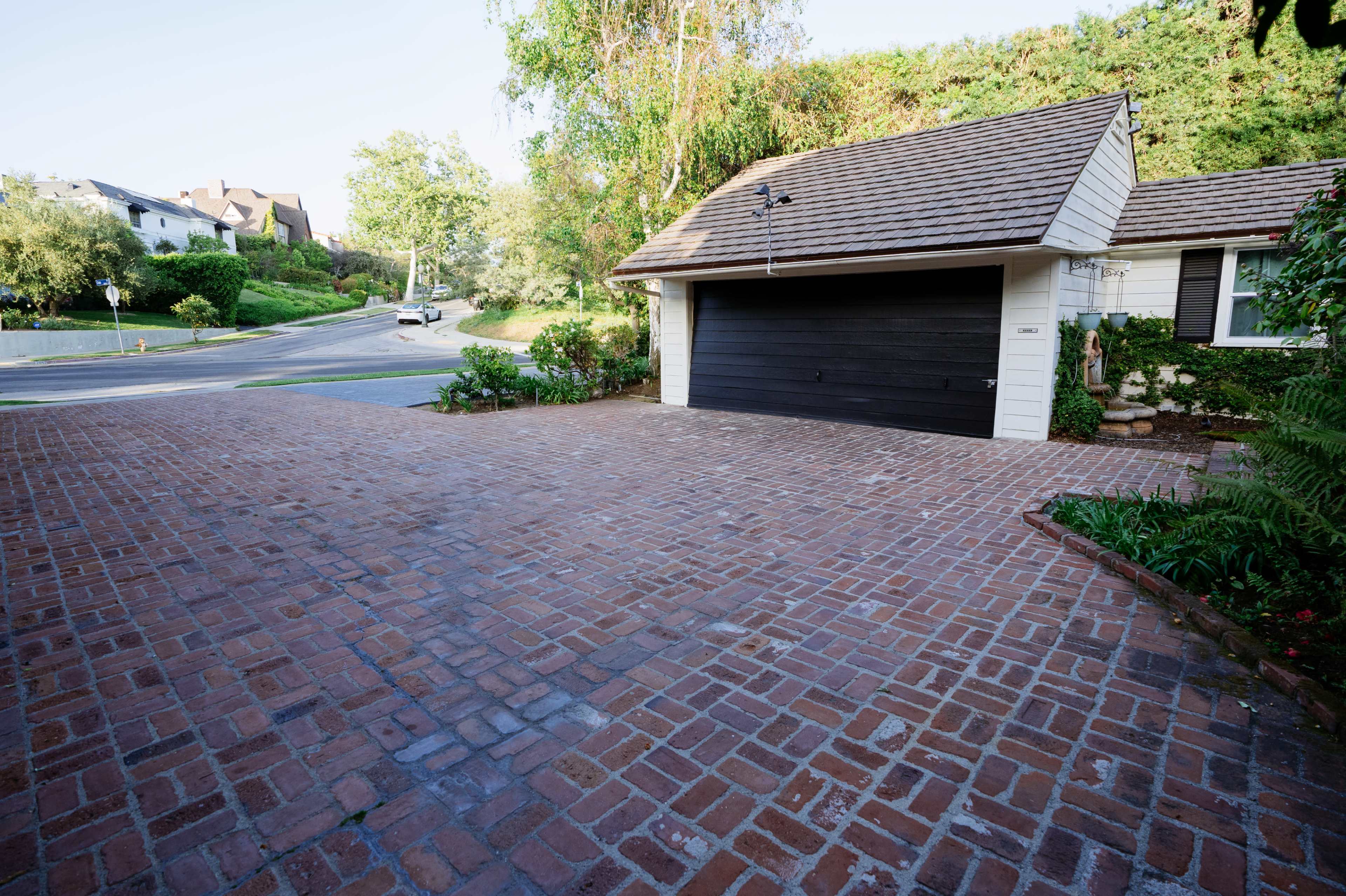The image shows a brick driveway leading to a garage nestled beside a suburban road.