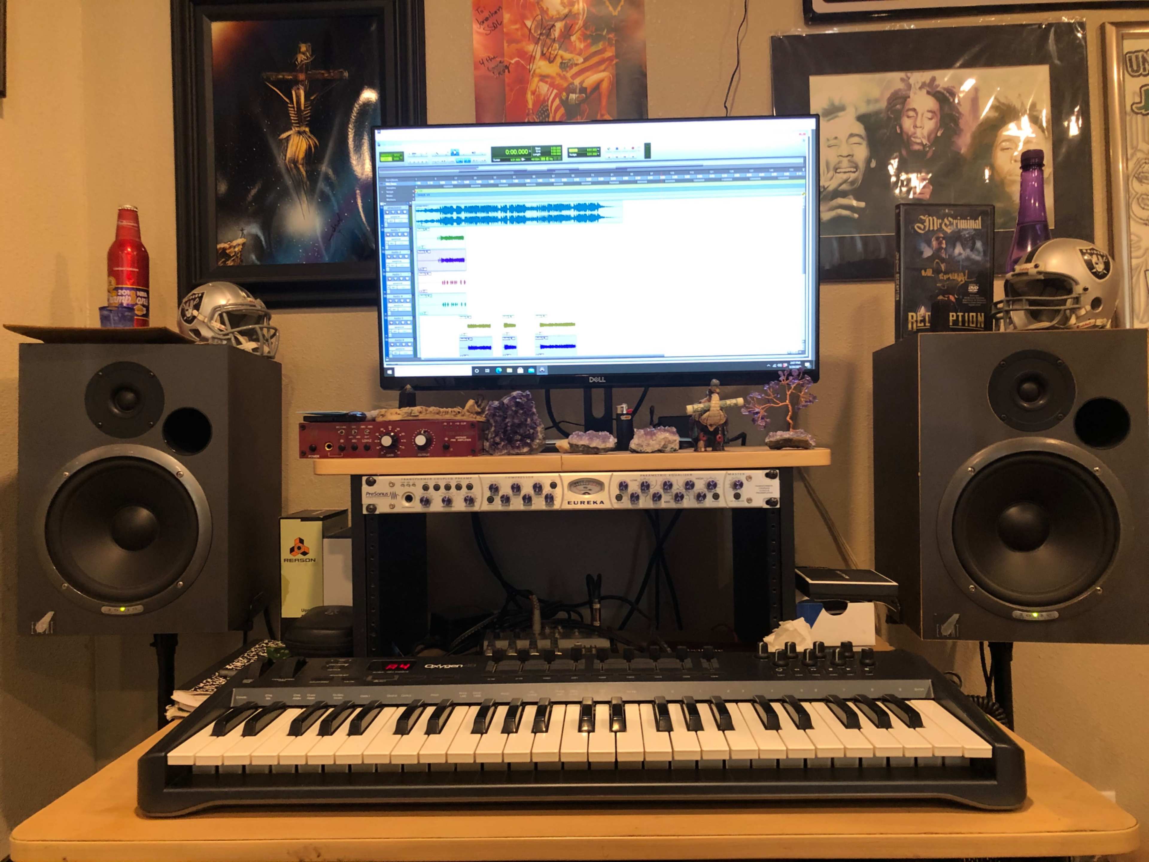 A desktop recording setup features a computer monitor displaying audio tracks, flanked by large speakers and a MIDI keyboard.