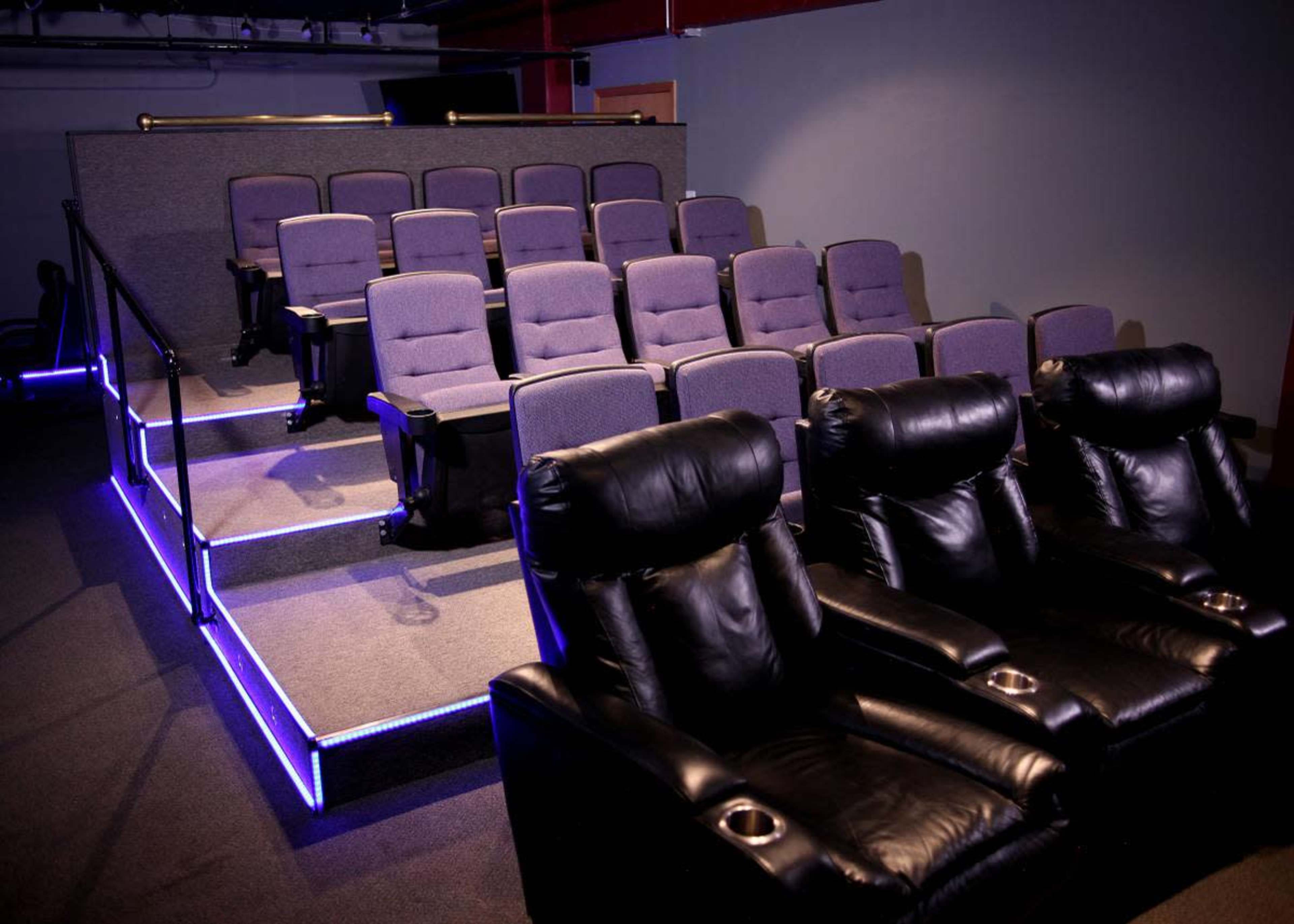 A small home theater with tiered seating comprising gray chairs and black recliners, illuminated by blue LED lights.