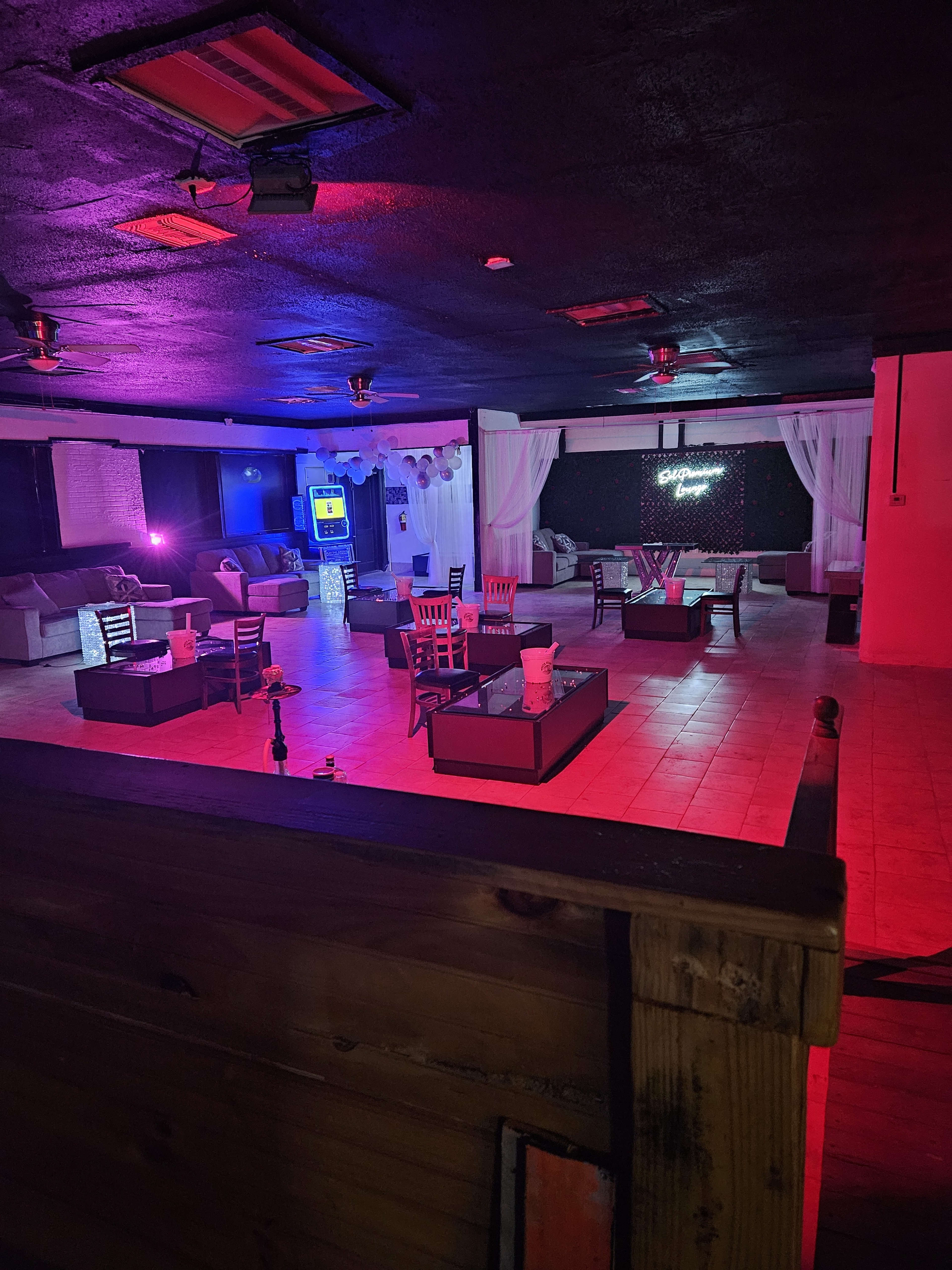 An empty lounge with seating arrangements, colorful lighting, and a bar area.