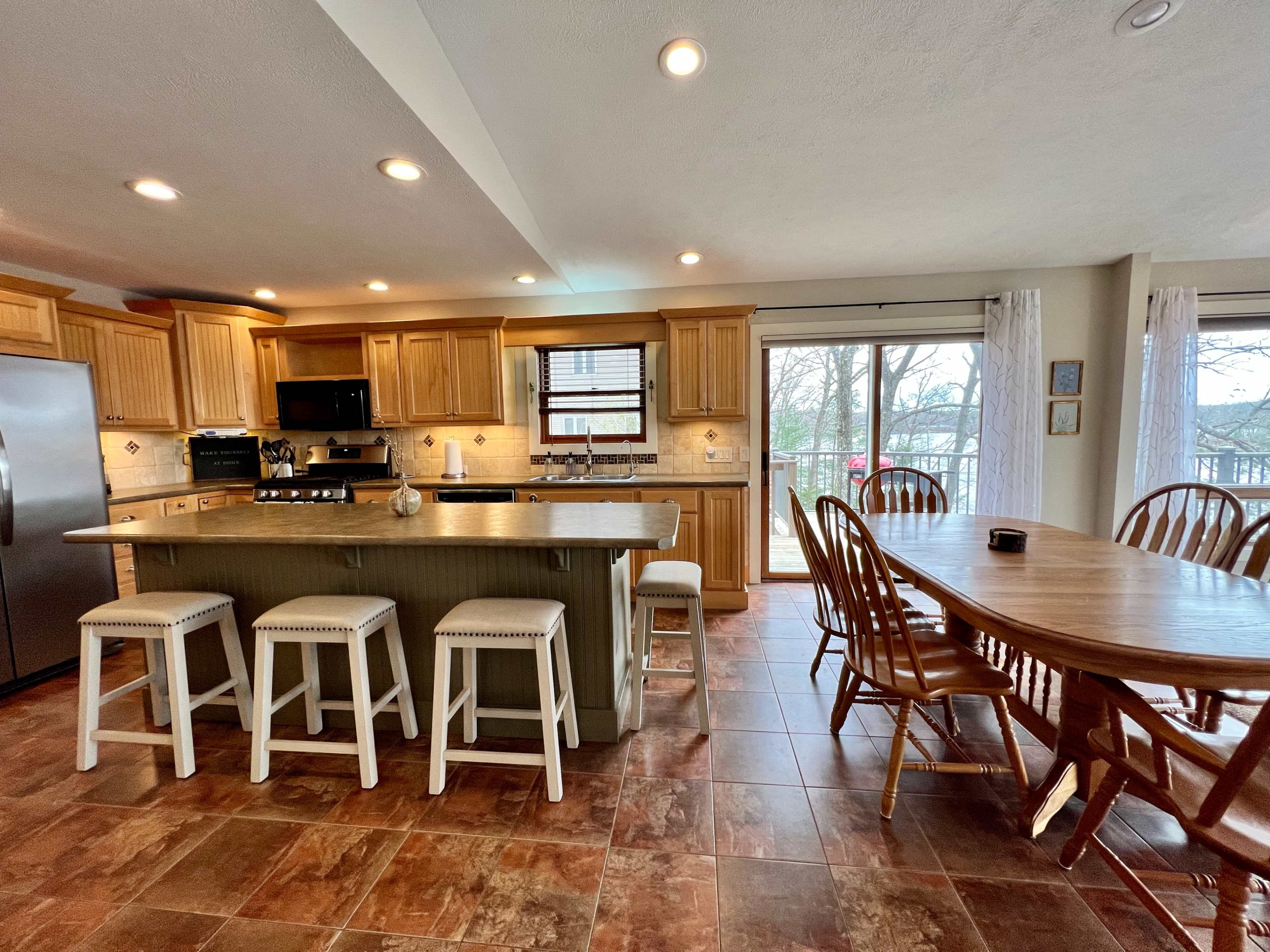 A spacious kitchen with wooden cabinets, a large island with seating, and a dining area featuring a round table by a large window.