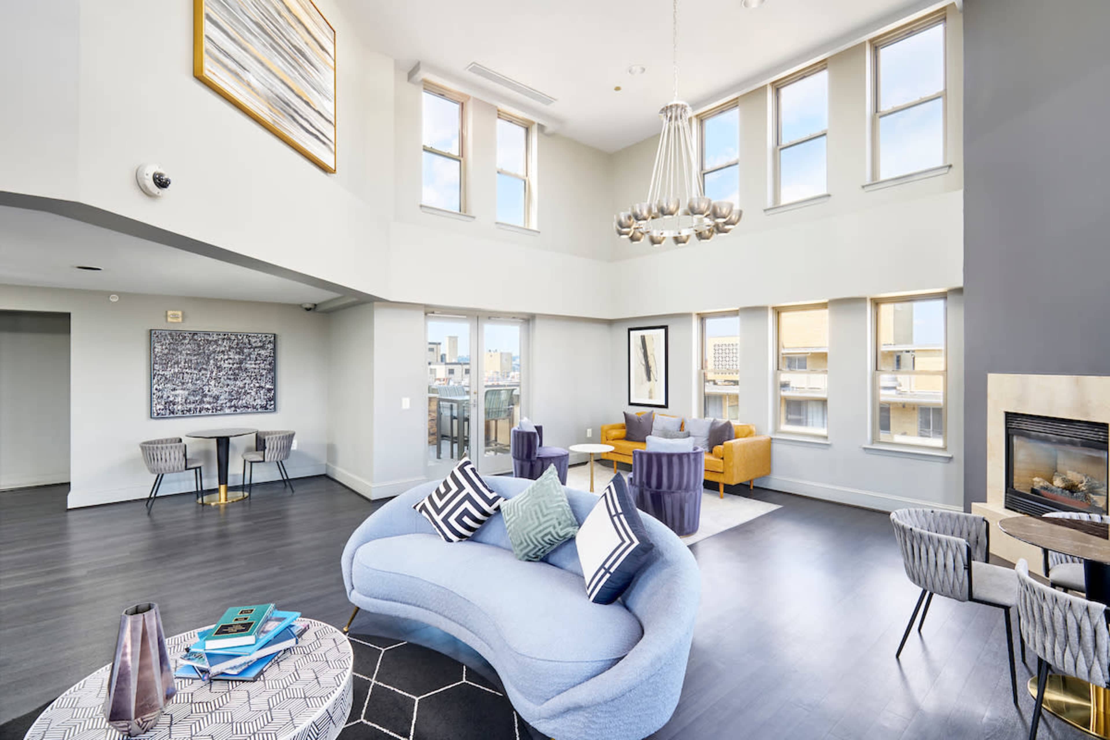 A modern living area with high ceilings, large windows, and a mix of stylish furniture including a curved blue sofa, yellow chairs, and a fireplace.