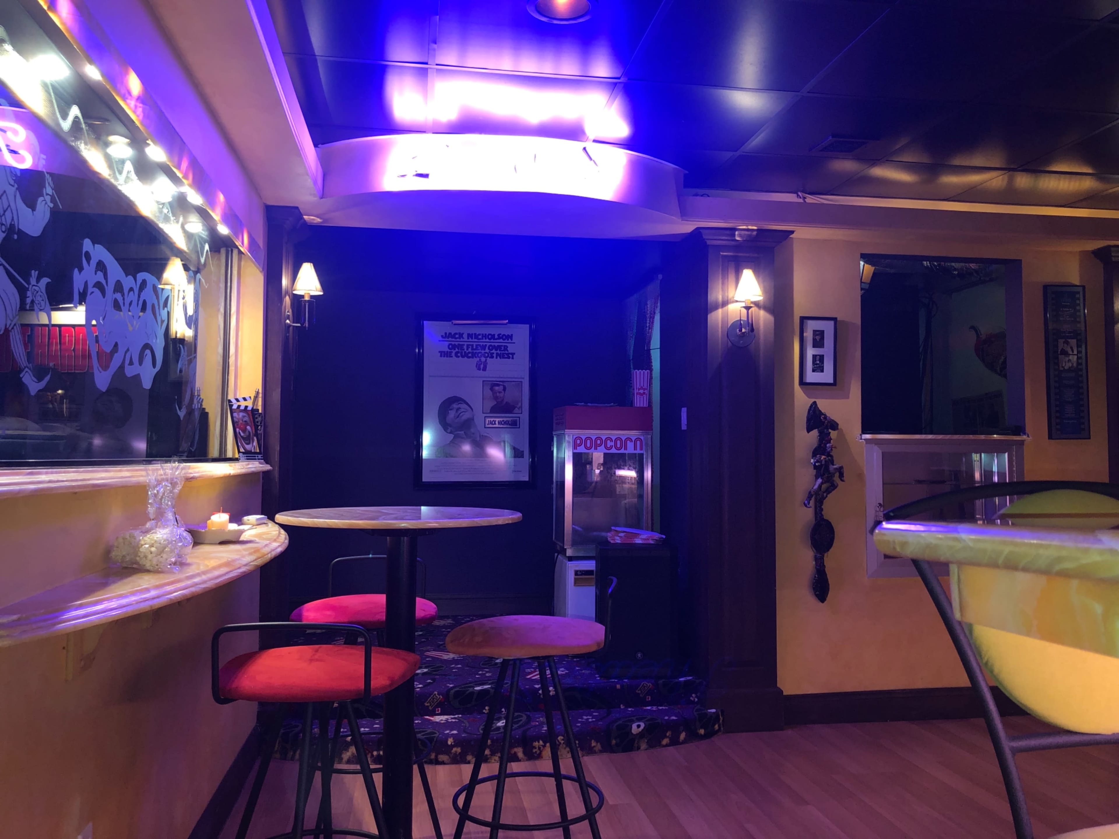 A dimly lit room with two tables and red stools, featuring a popcorn machine and colorful decorations on the walls.