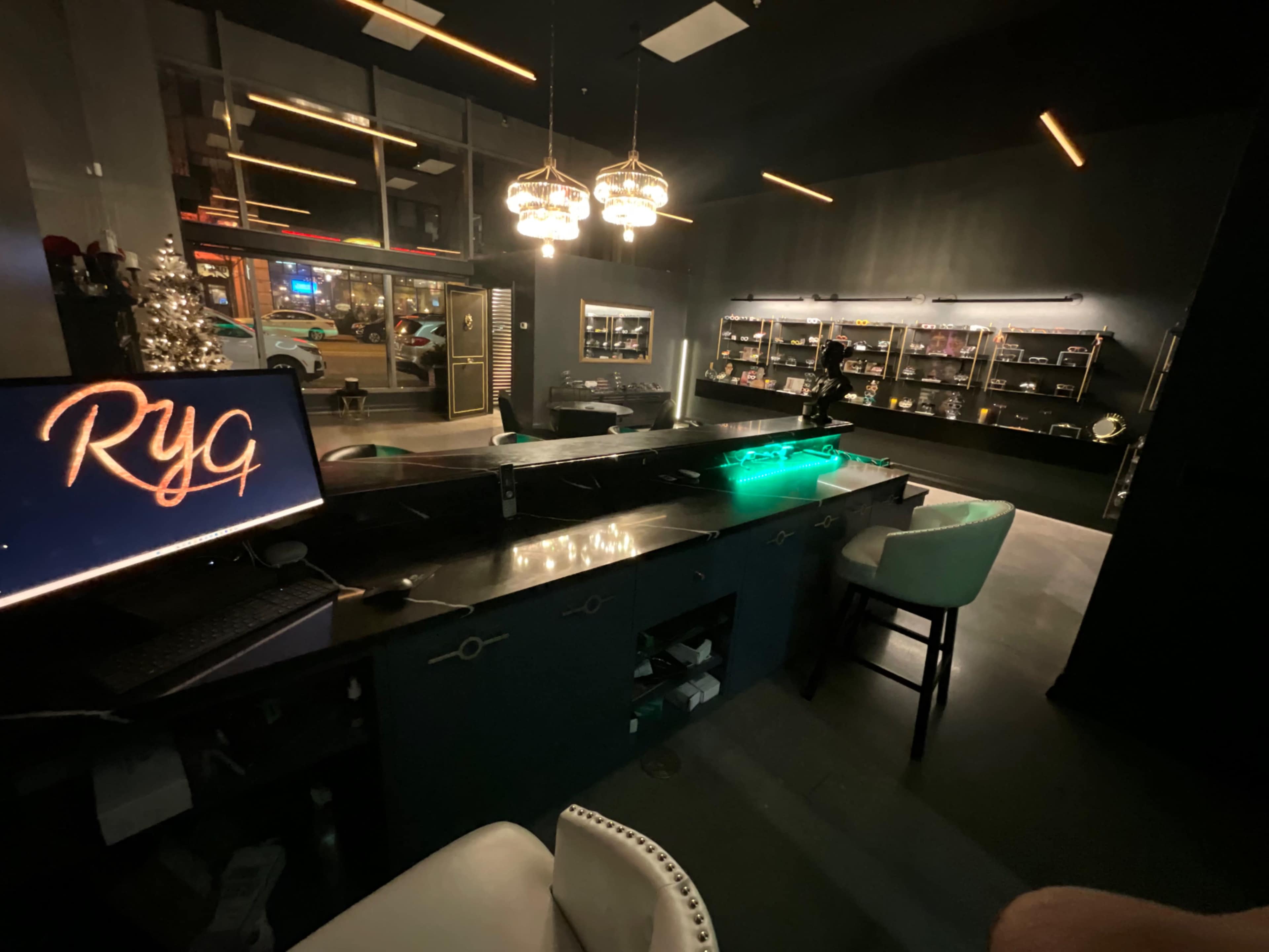 A dimly lit modern bar area with a sleek counter, illuminated by pendant lights, and shelves displaying various items in the background.