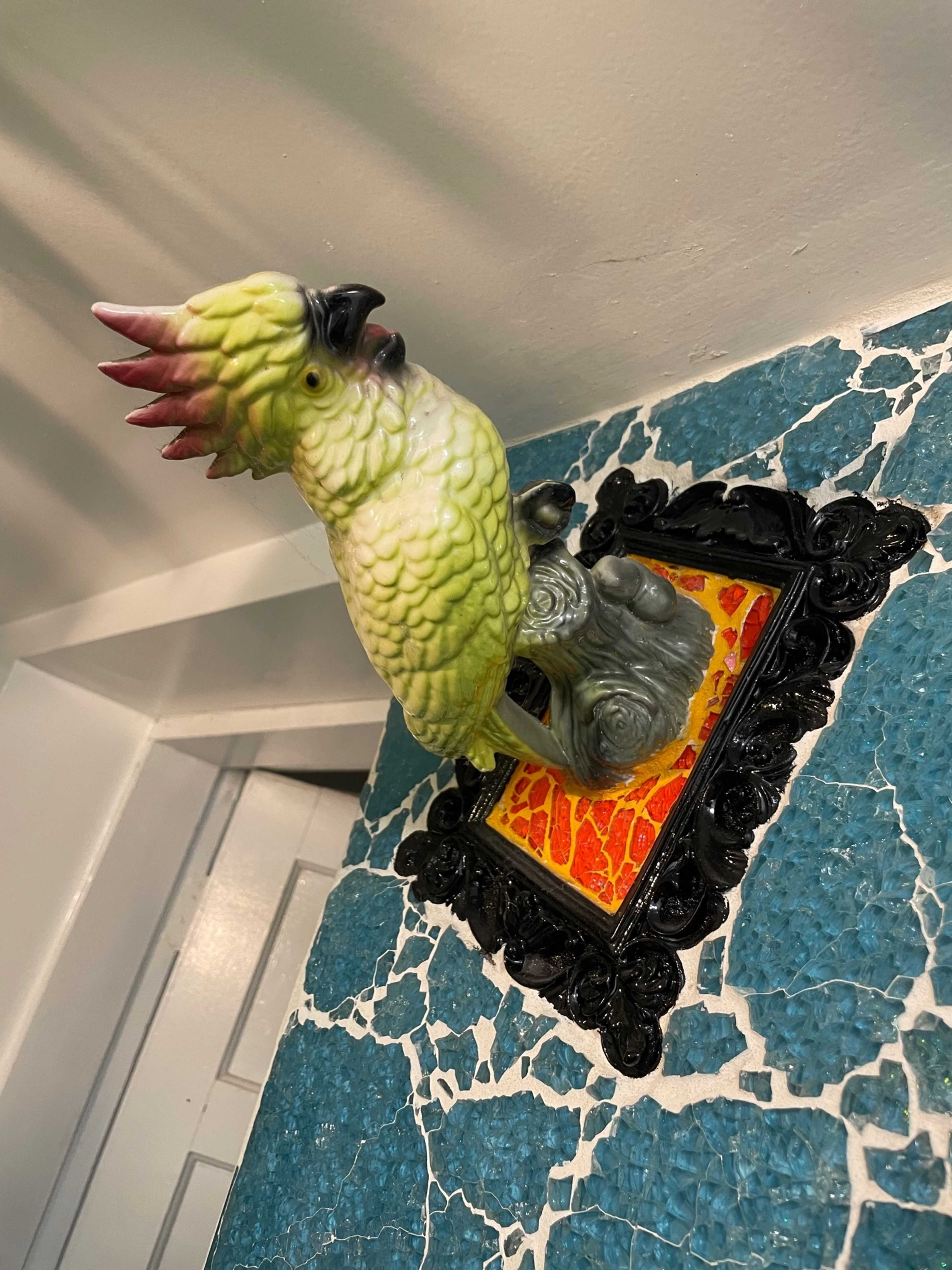 A ceramic parrot sculpture is mounted on a decorative wall plaque featuring an orange and yellow design.