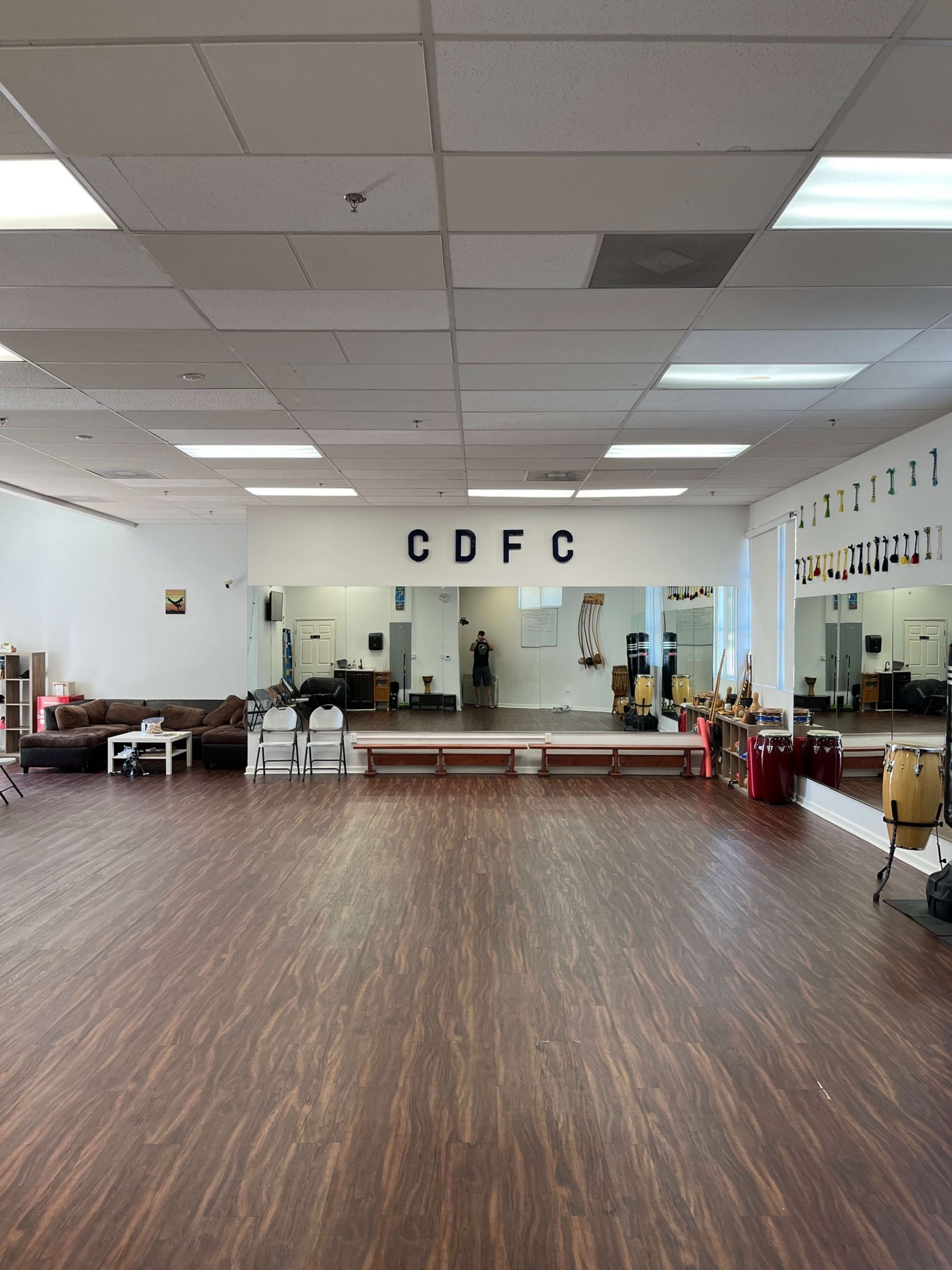 The room features a wooden floor, mirrors on one wall, and various percussion instruments along with seating areas.