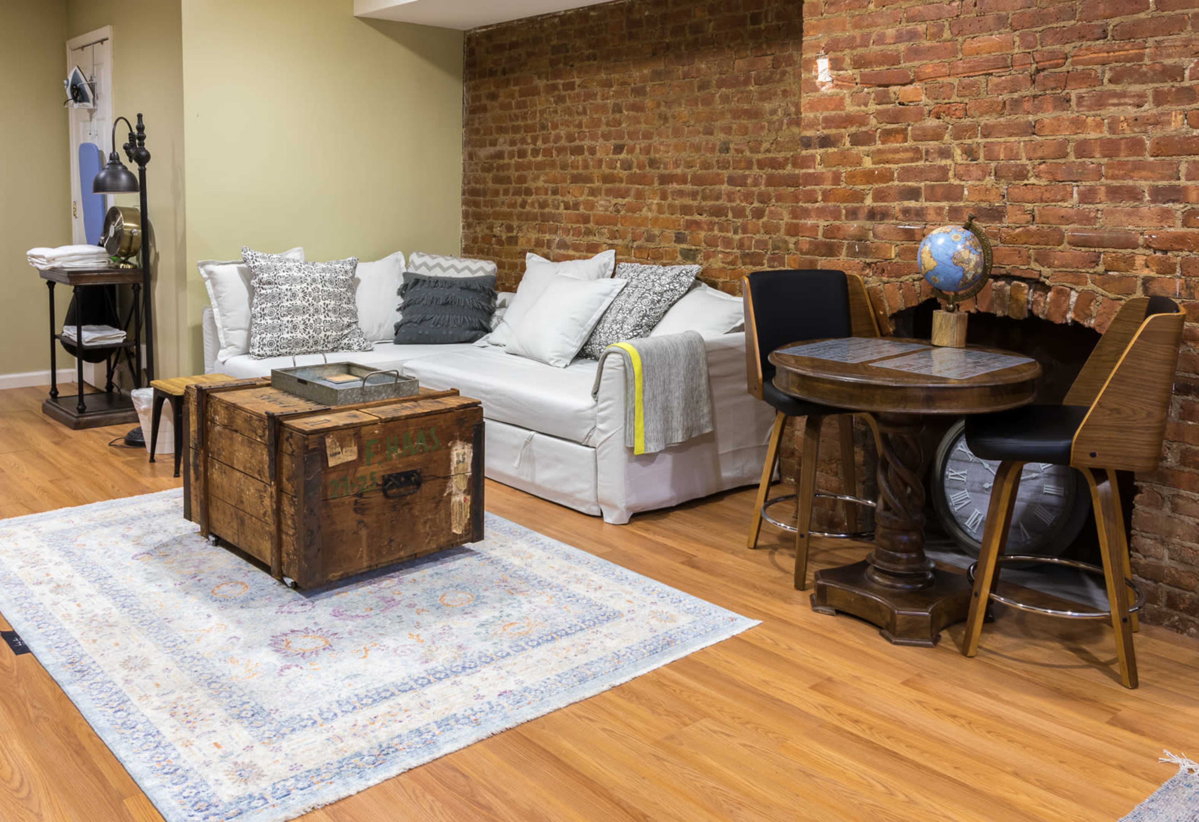 A cozy living space featuring a white sofa adorned with decorative pillows, a rustic wooden coffee table, and a small dining area with a globe and a round table.
