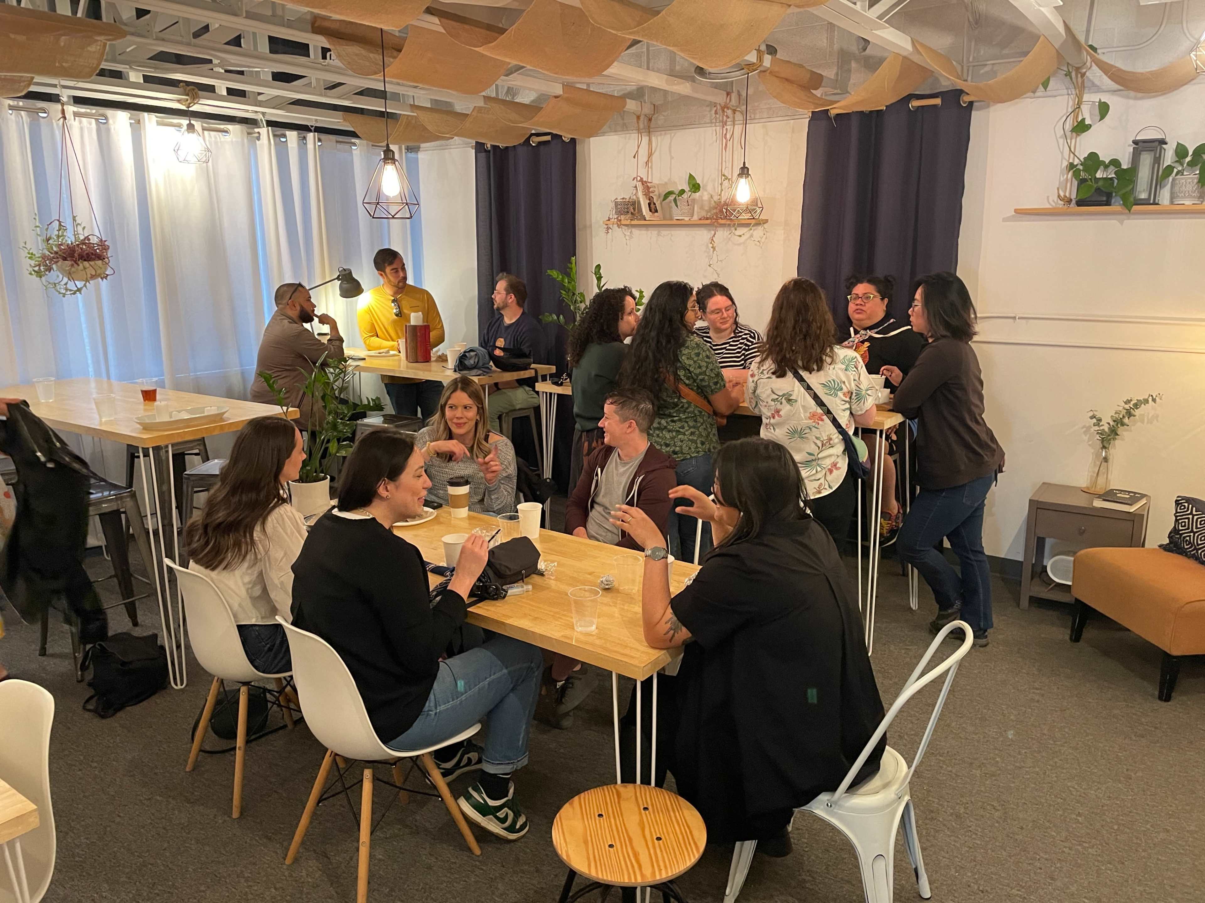 A group of people engages in conversation and dining at tables in a cozy, well-lit café setting.