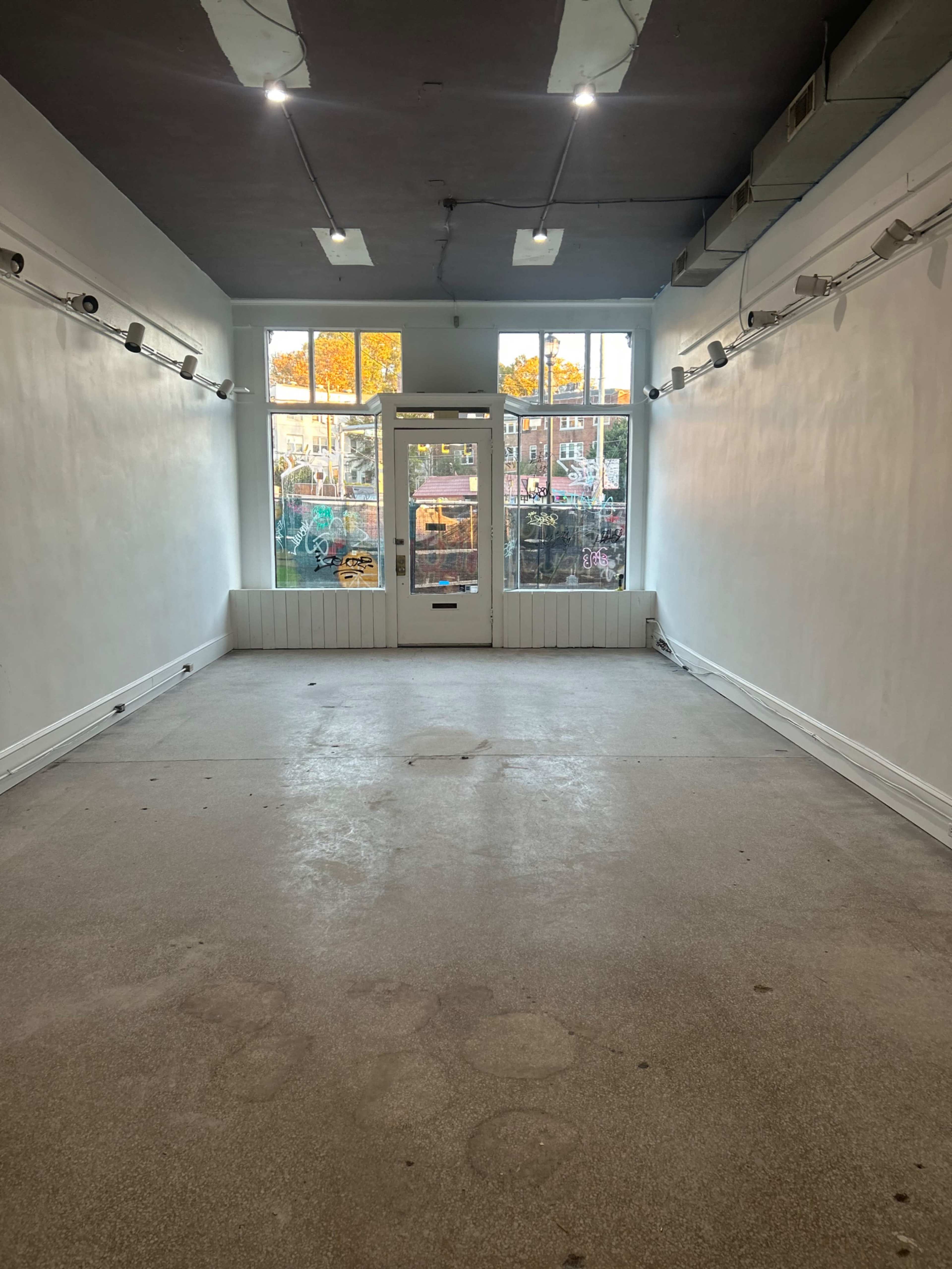 The image shows an empty retail space with white walls and large windows at the front.