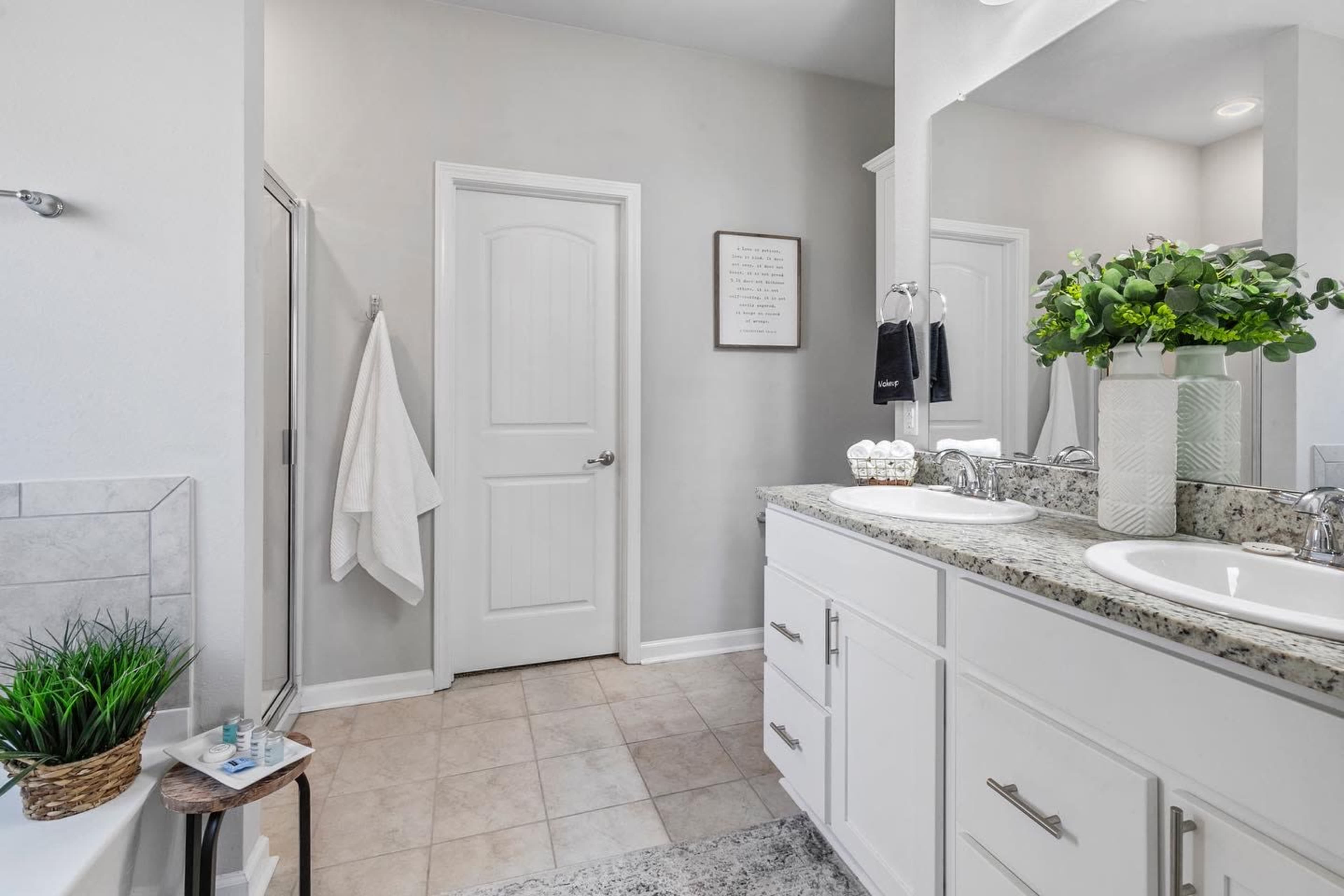A modern bathroom with a double sink vanity, light grey walls, and a glass shower enclosure.