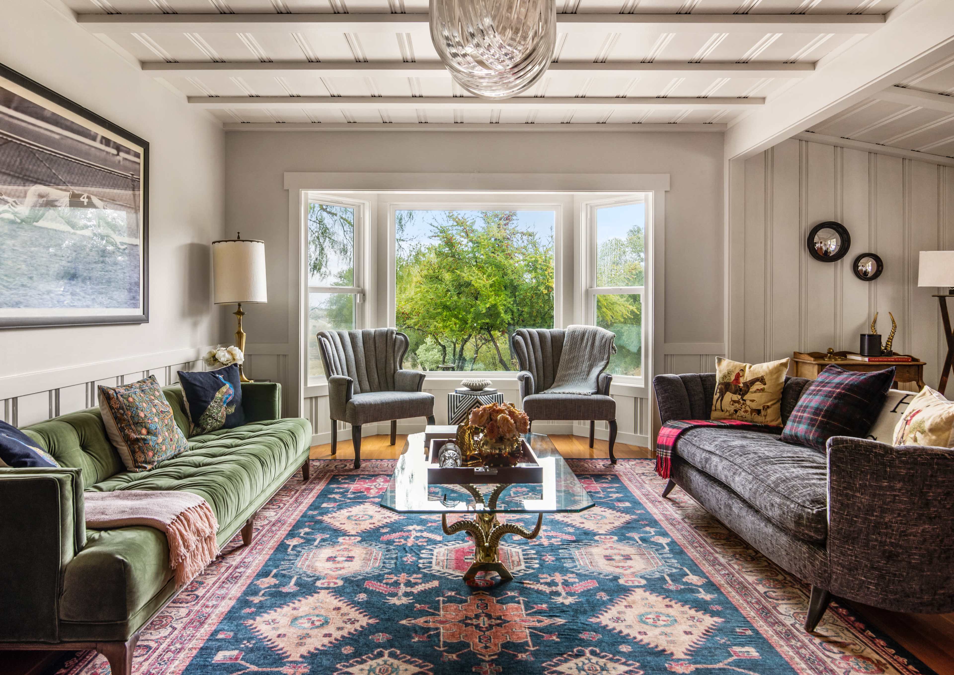 A living room features green and gray sofas, a glass coffee table, and large windows overlooking a lush landscape.