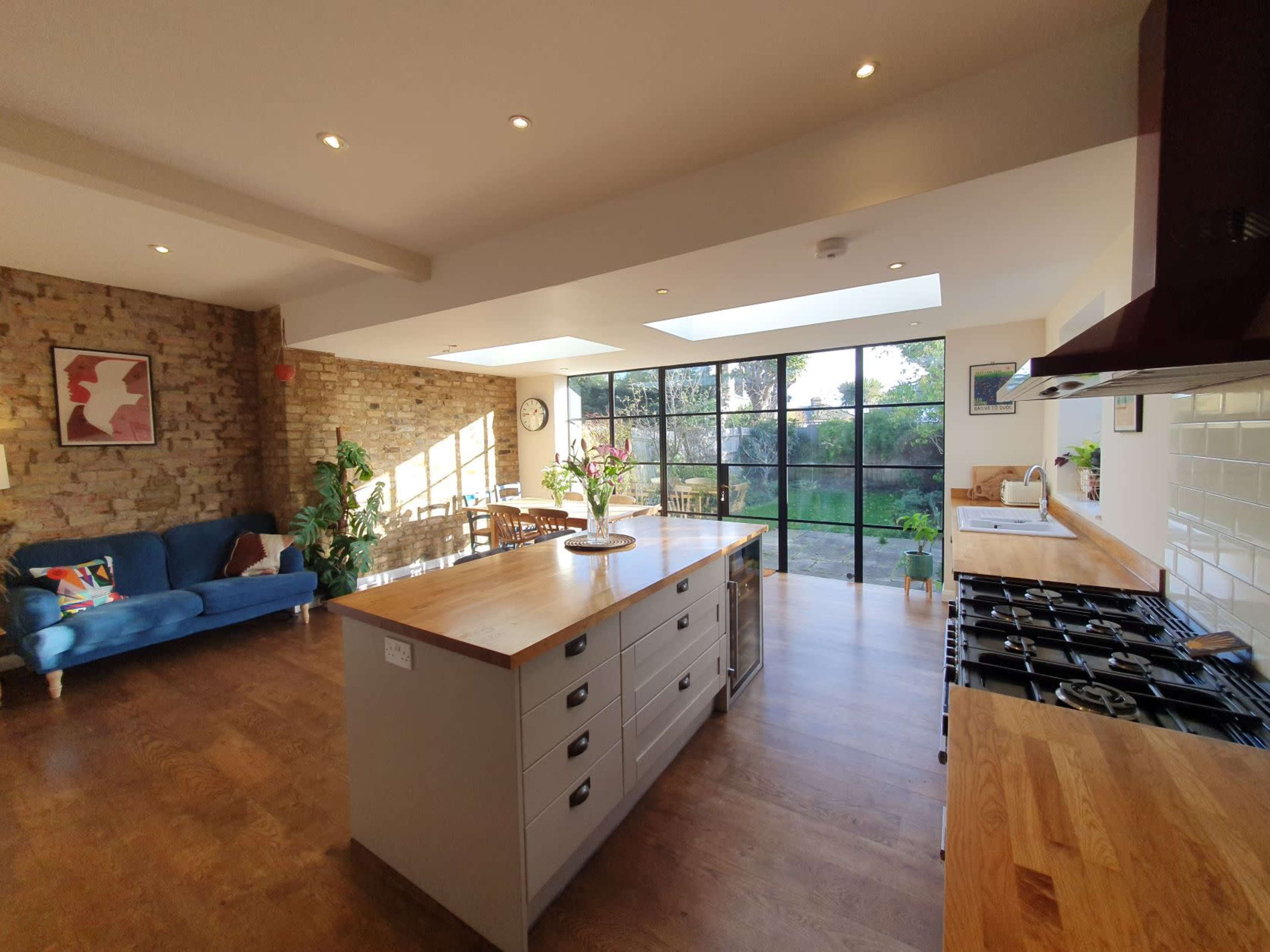A modern kitchen with a wooden island, a gas stove, and large windows overlooking a garden.