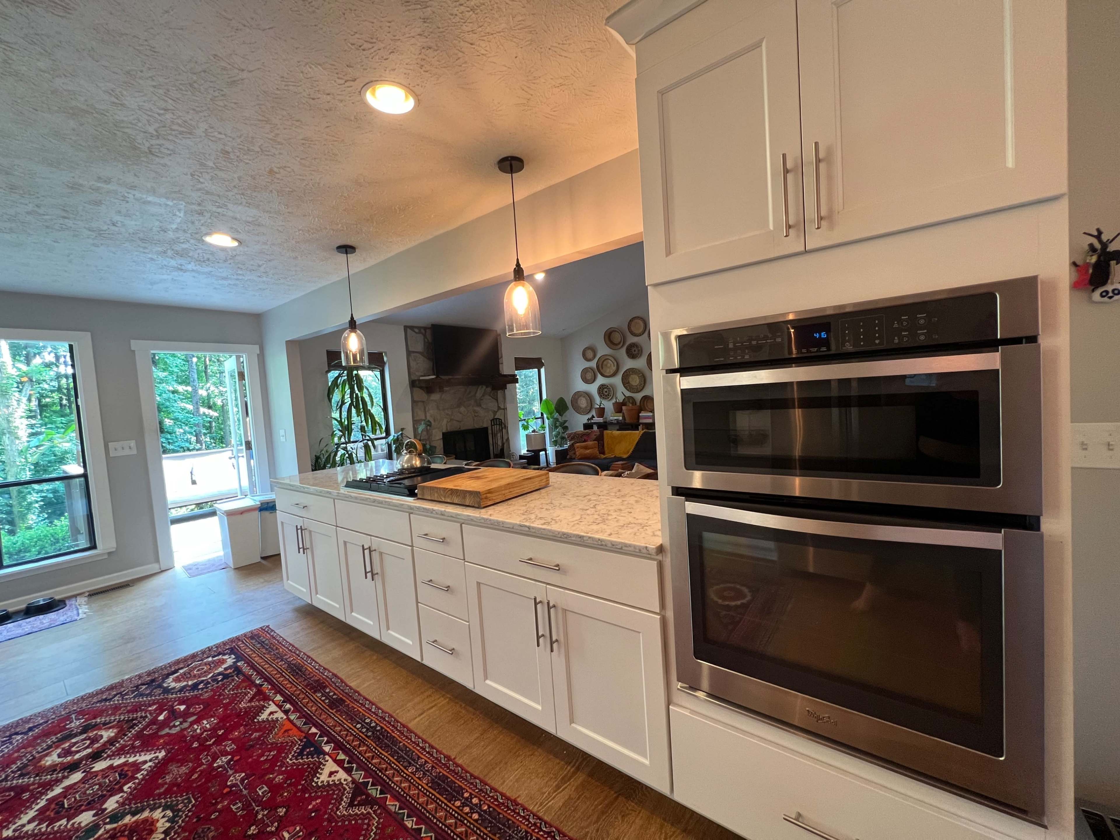 A modern kitchen features white cabinetry, stainless steel double ovens, and a large countertop with a cutting board.