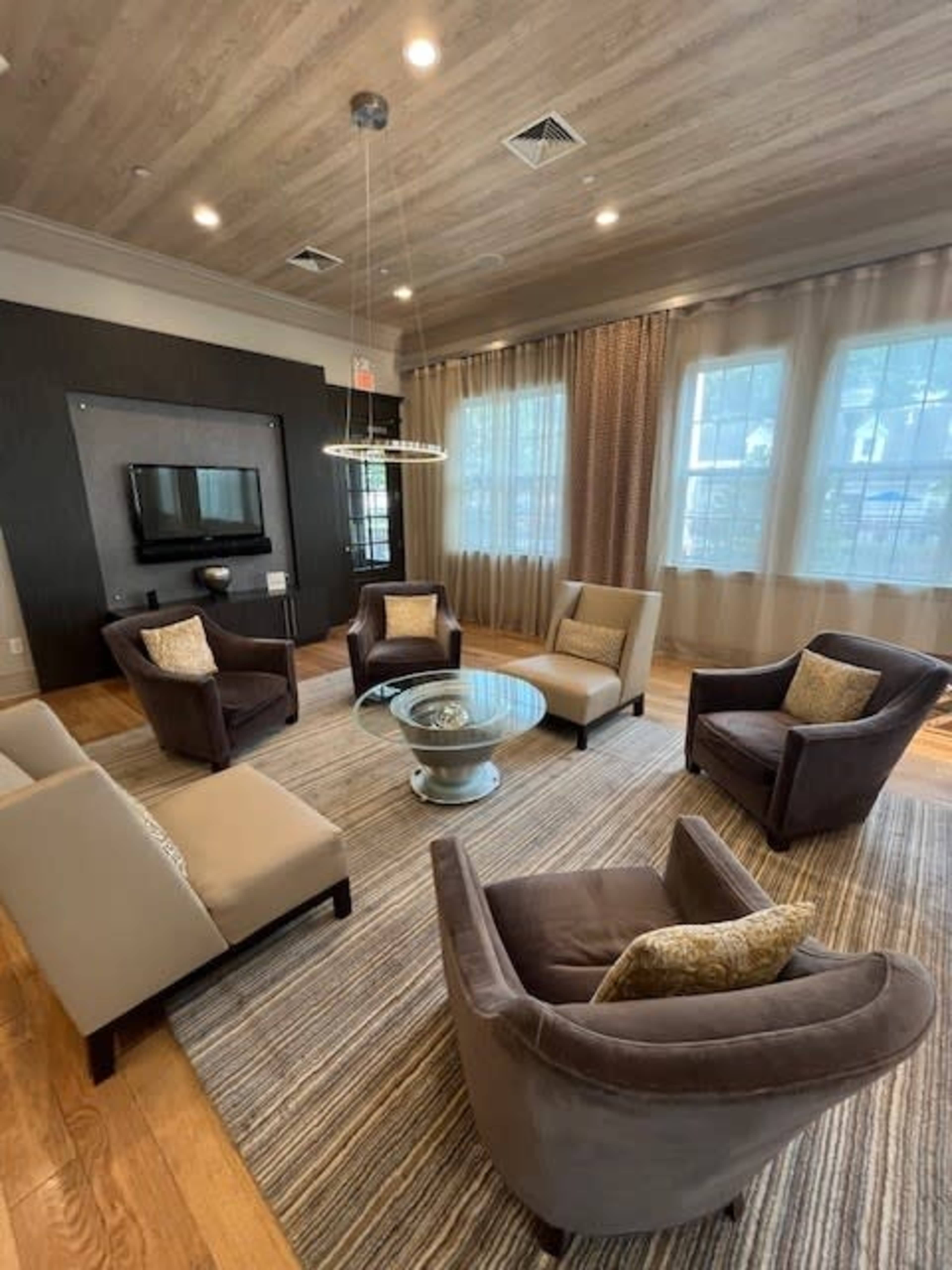 A modern living room with two armchairs and a sofa arranged around a glass coffee table on a striped rug, with a television mounted on the wall behind.