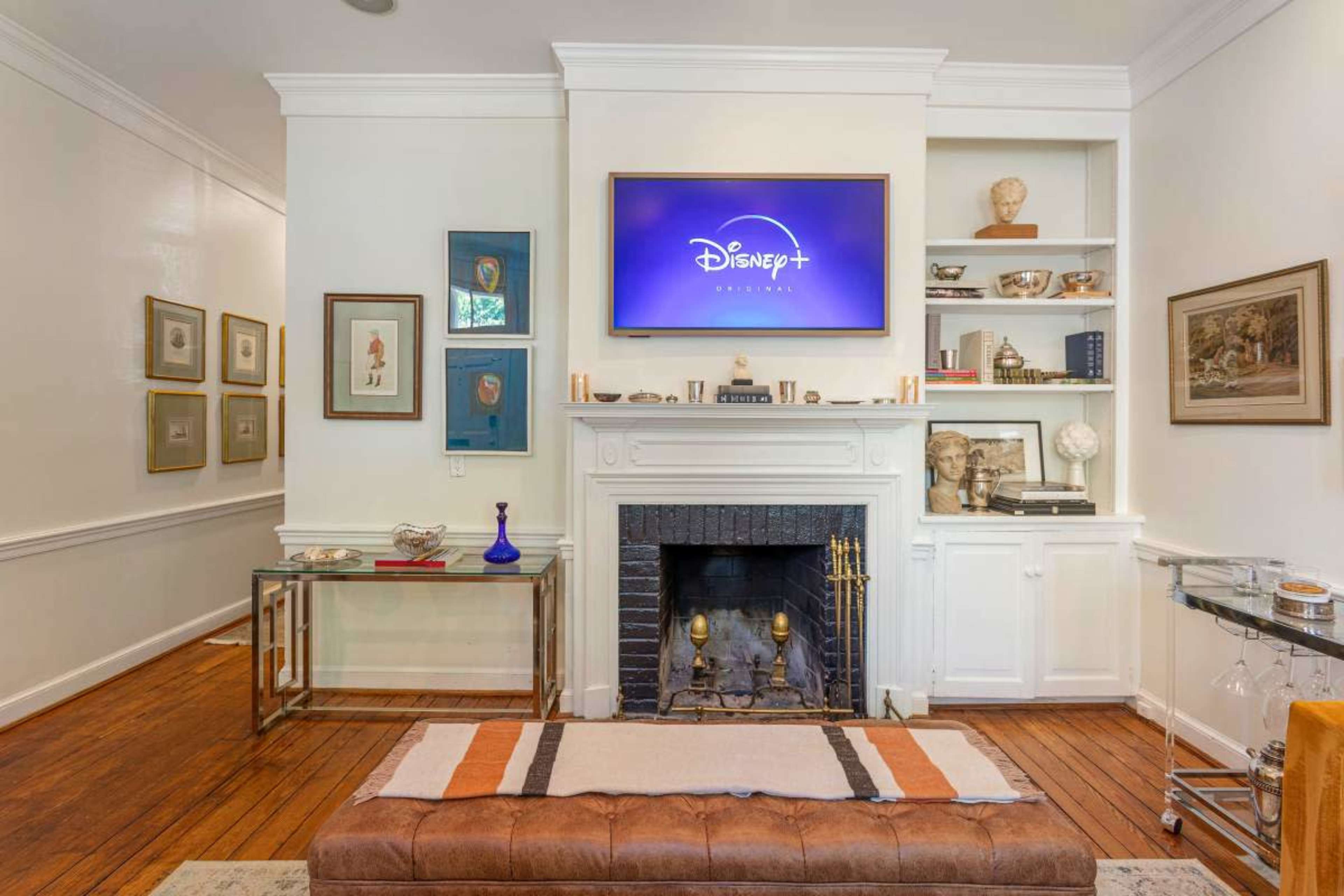 The image shows a living room with a television mounted above a fireplace, accented by shelves displaying various decorative items and framed artwork on the walls.