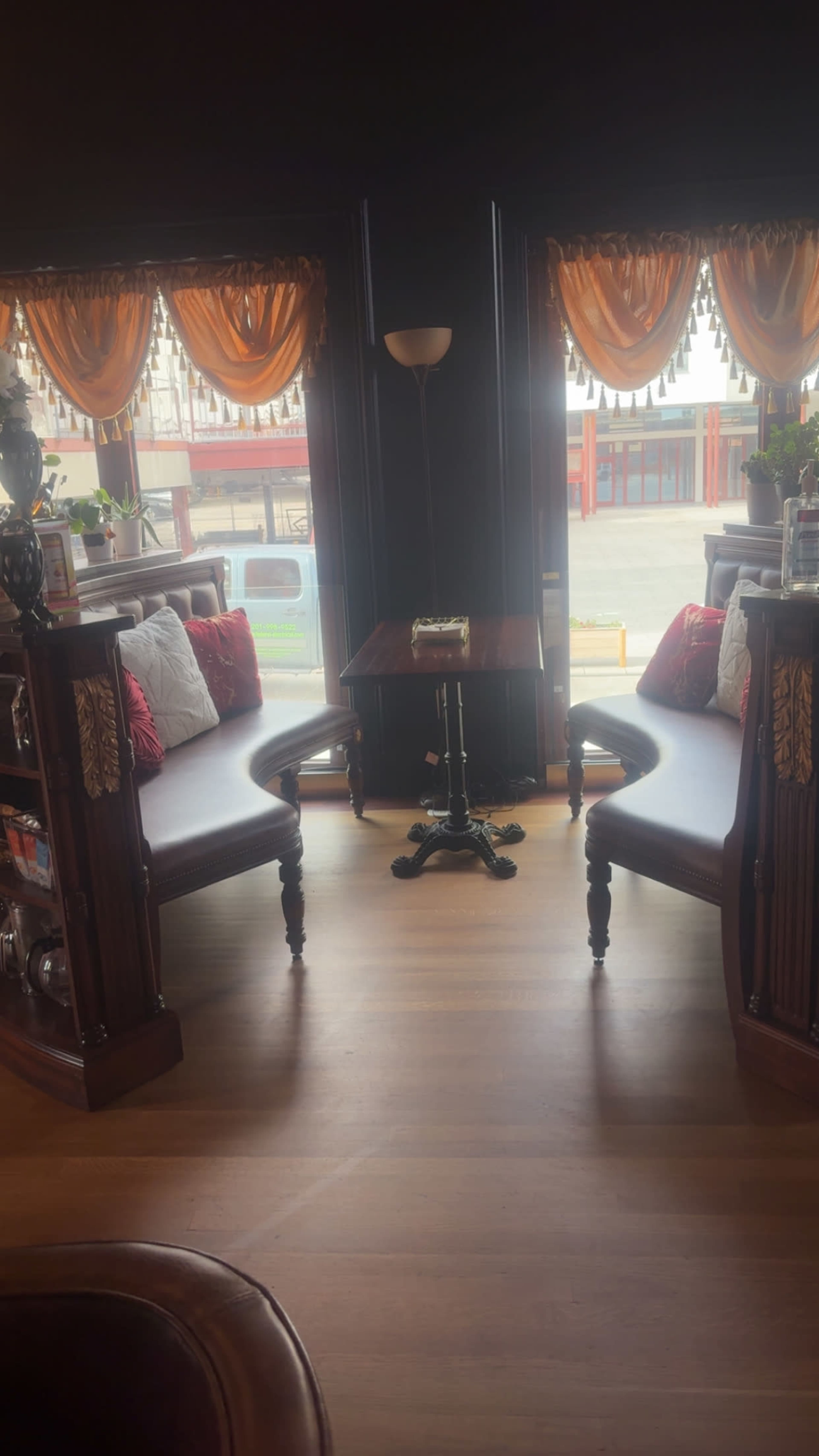 The image features two curved wooden benches facing each other, positioned around a small table in a well-lit area with large windows adorned with orange drapes.