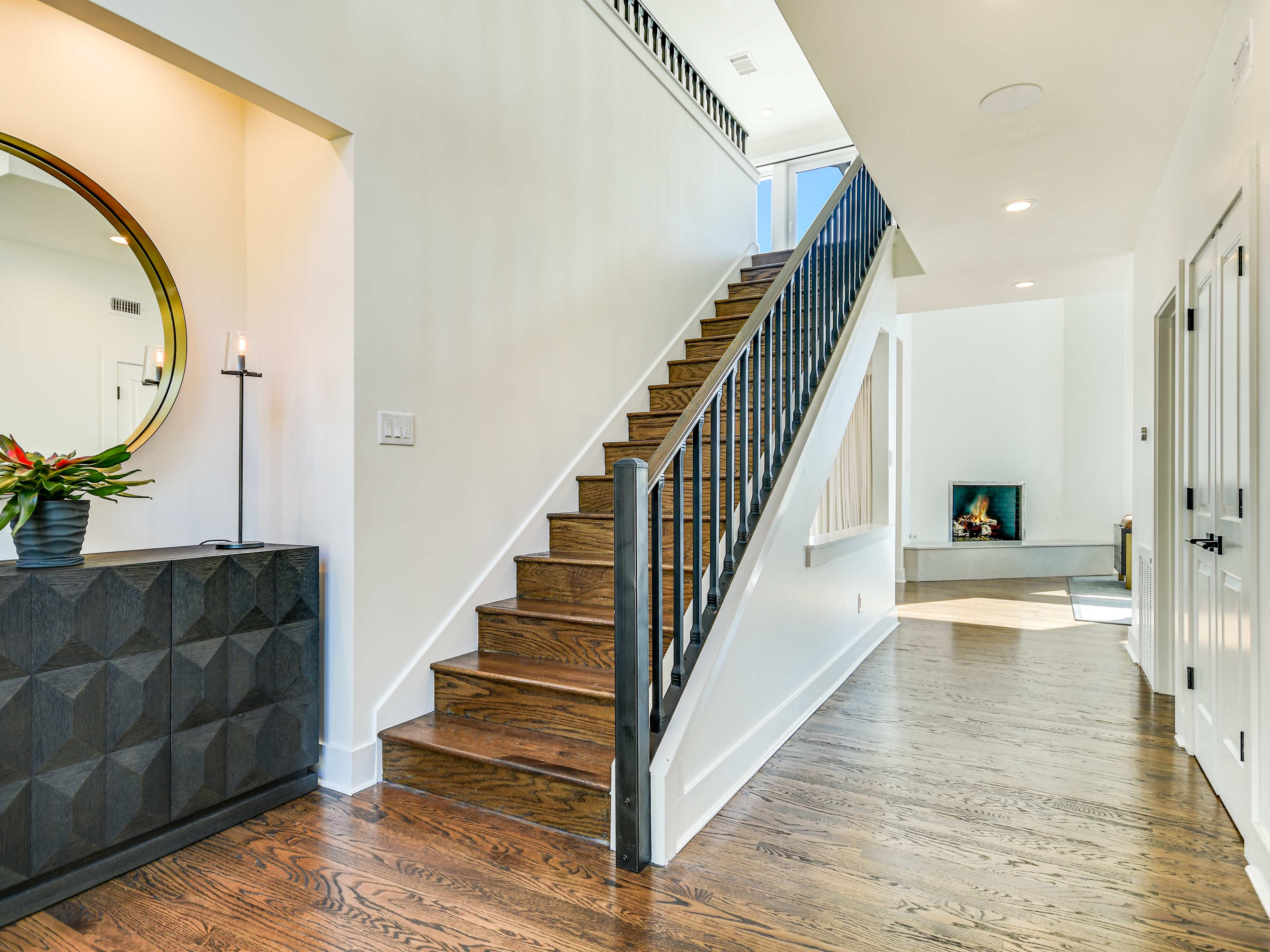 The image shows a modern foyer with a staircase leading to an upper level, a fireplace, and a geometric console table.